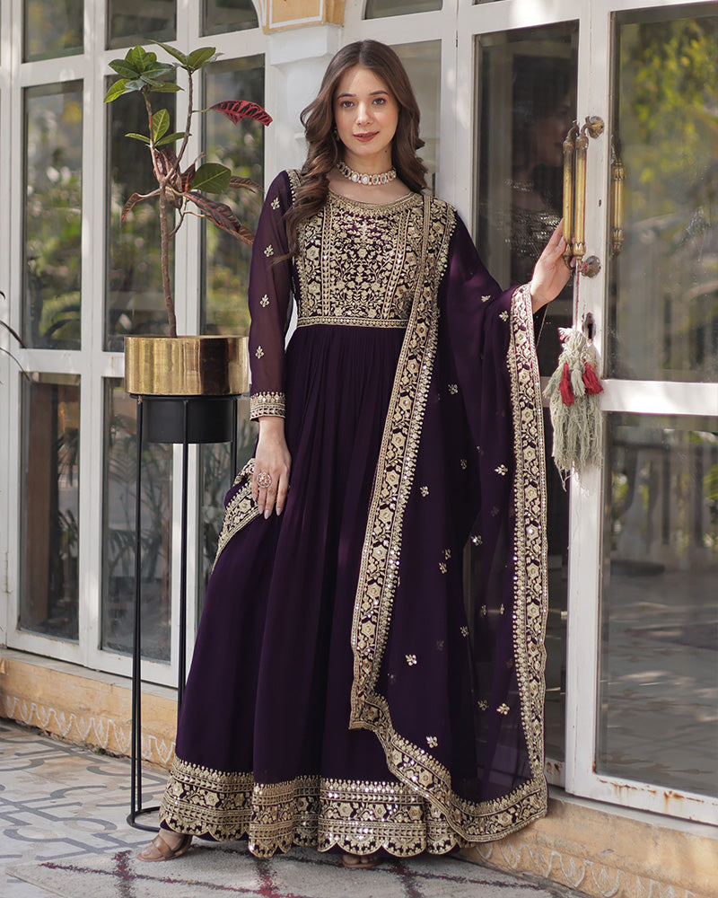 Woman in a dark purple traditional outfit with gold embroidery standing indoors.