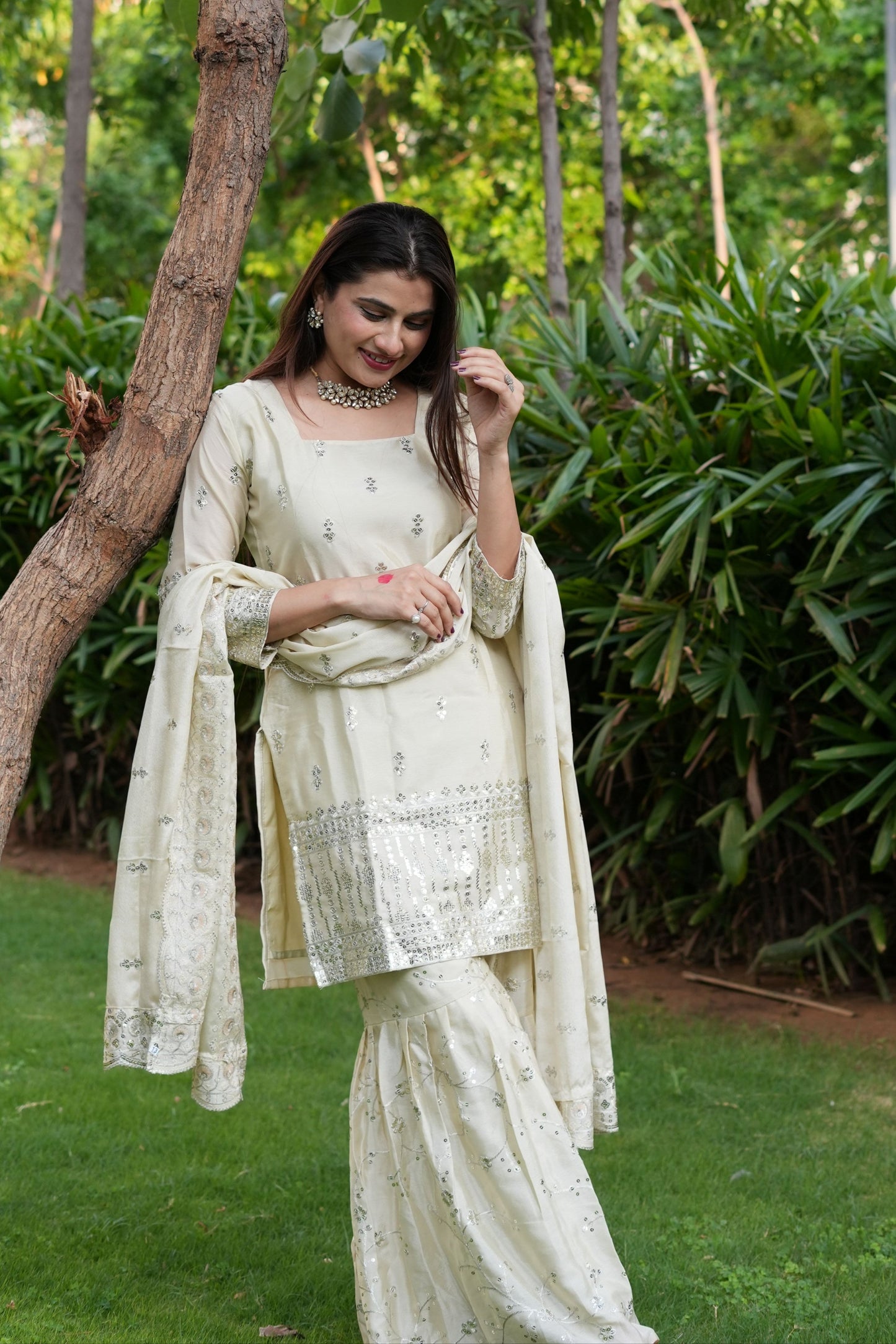 Woman in a traditional outfit standing outdoors with greenery in the background