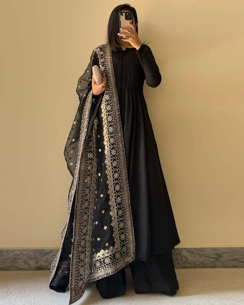 Person wearing a black outfit with a patterned scarf against a beige wall.