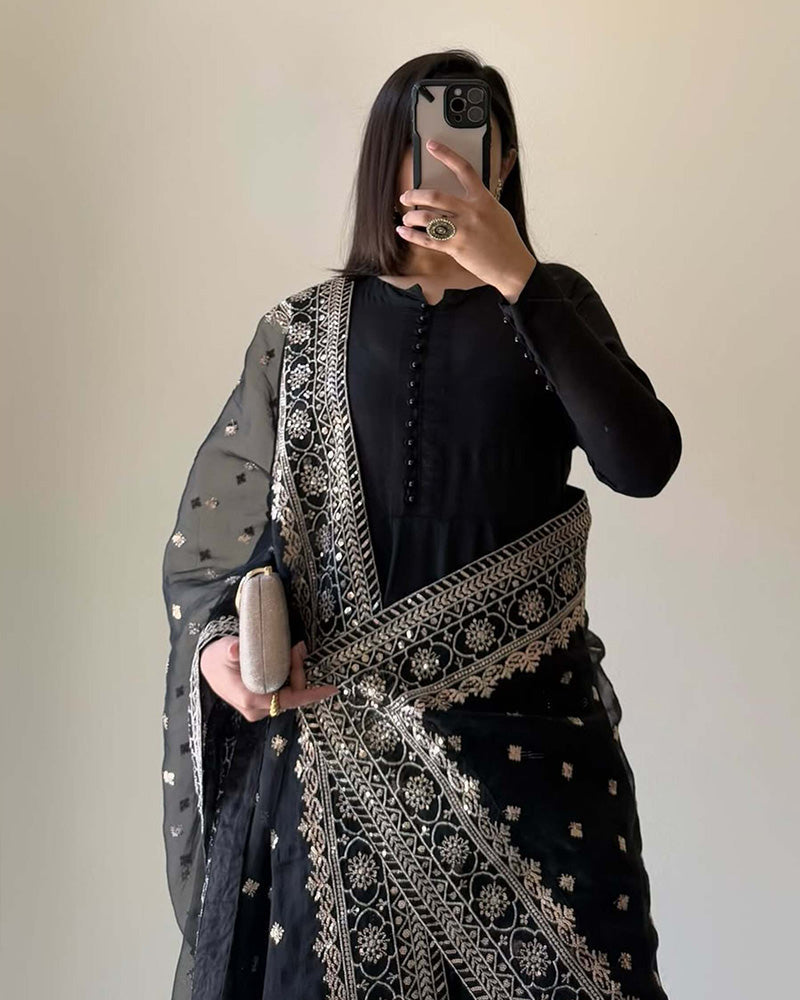 Person wearing a black outfit with intricate patterns, holding a phone.