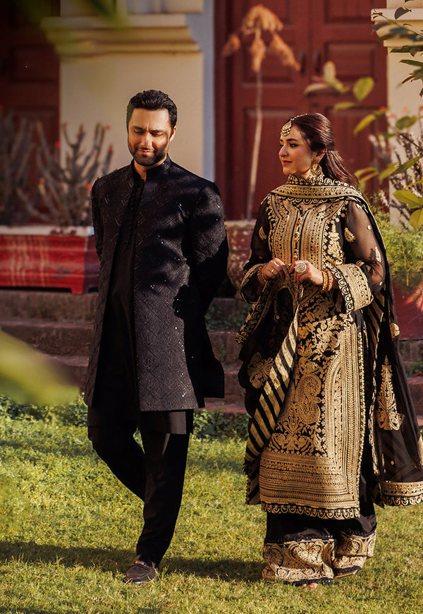 Man and woman in traditional attire walking outdoors with a decorative background