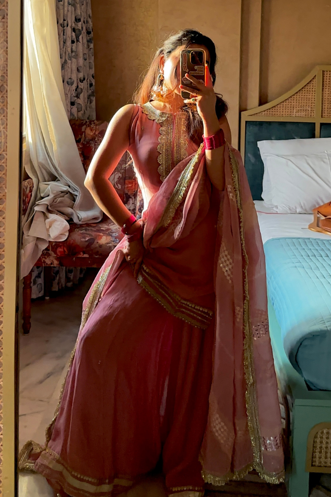 Person wearing a pink saree with gold details in a bedroom setting.