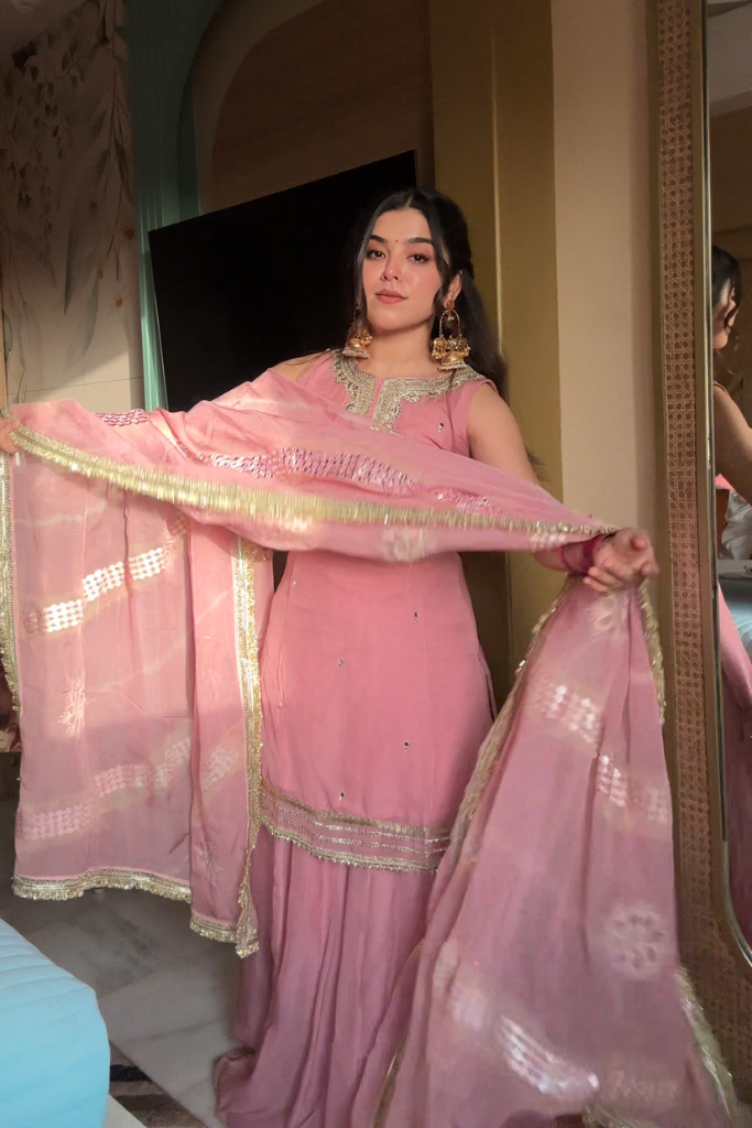 Woman in a pink traditional outfit with a dupatta, standing in a room.