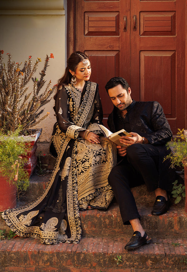 Man and woman in traditional attire sitting on steps with a wooden door in the background.