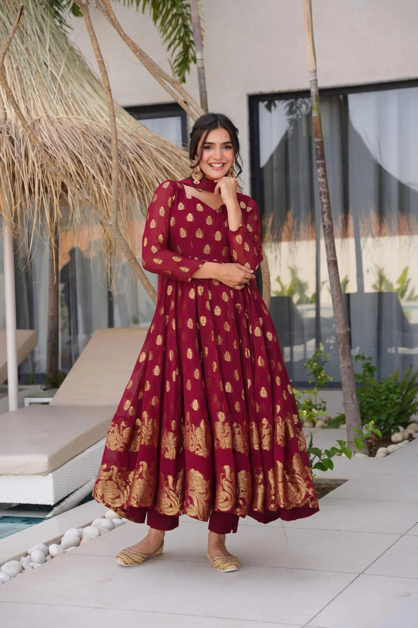 Woman in a red and gold dress standing outdoors near a poolside area.