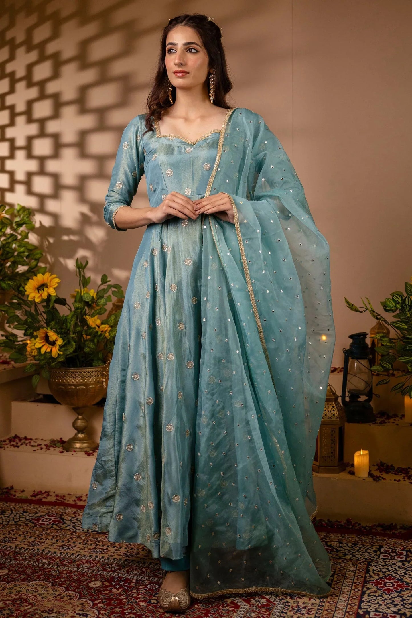 Woman in a light blue traditional outfit with a matching dupatta, standing in a decorated indoor setting.