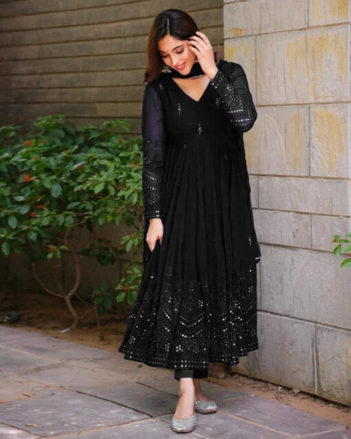 Woman wearing a black dress with sequin details standing against a stone wall.