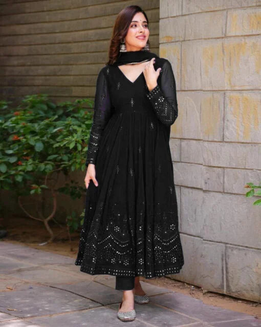 Woman wearing a black dress with intricate designs standing outdoors.