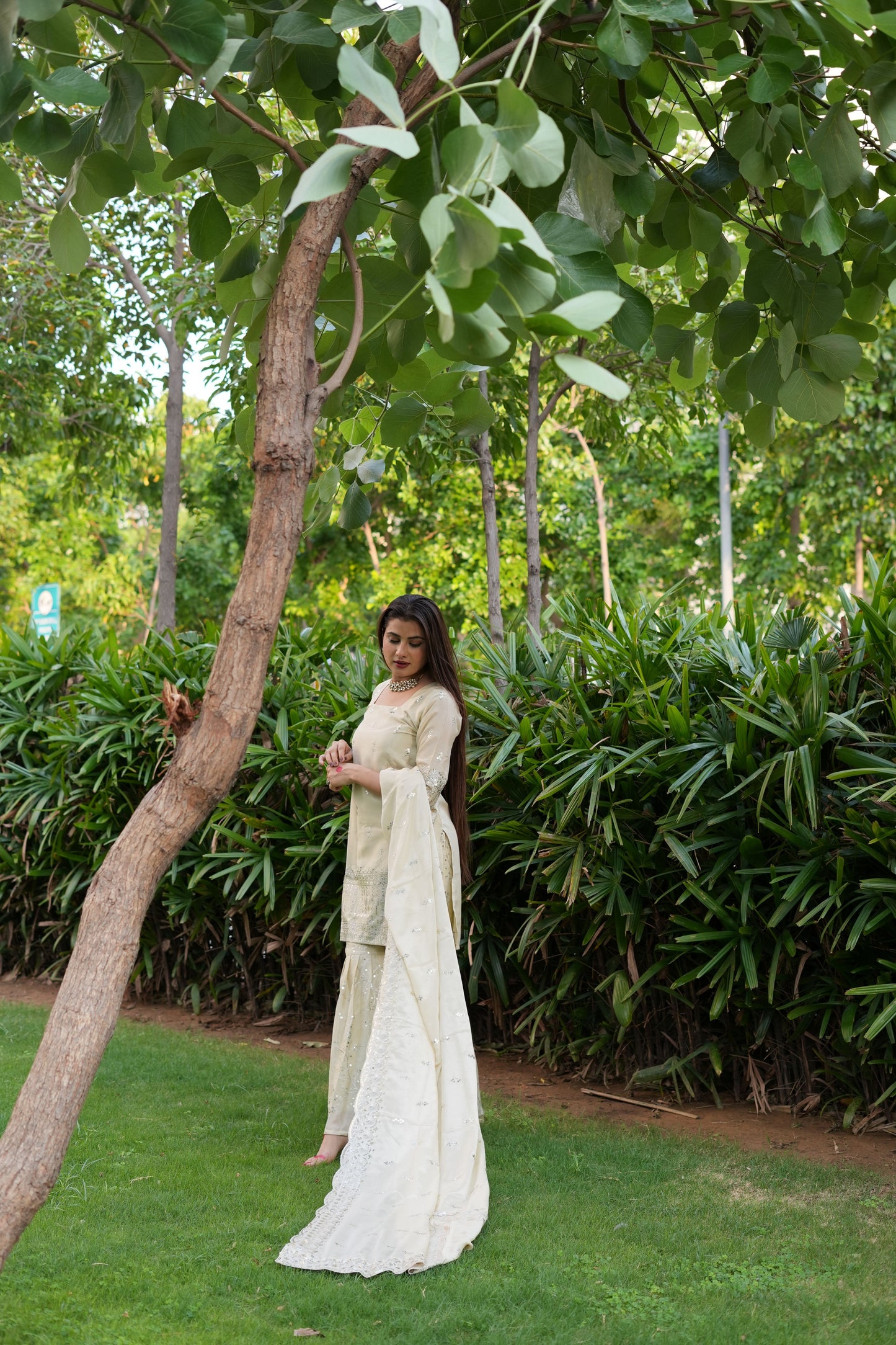 Woman in a white traditional outfit standing under a tree with greenery around