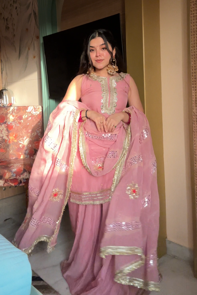 Woman in a pink saree with gold details indoors