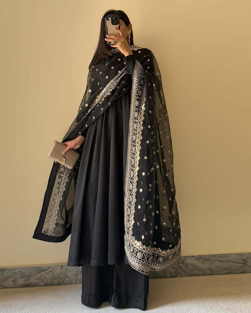 Person wearing a black traditional outfit with a matching dupatta against a beige background