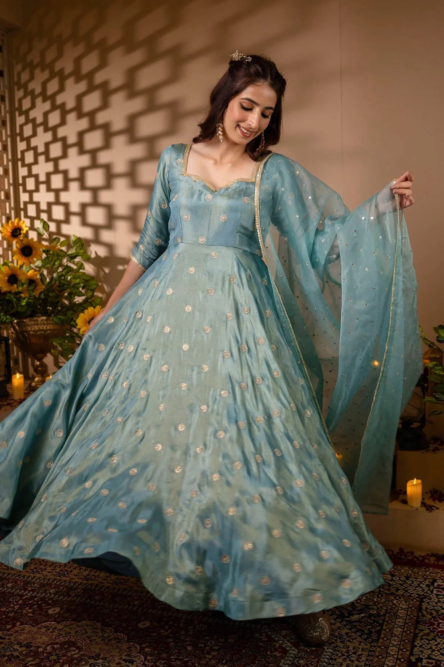 Woman in a light blue traditional outfit with a sheer dupatta, standing against a warm-toned wall.