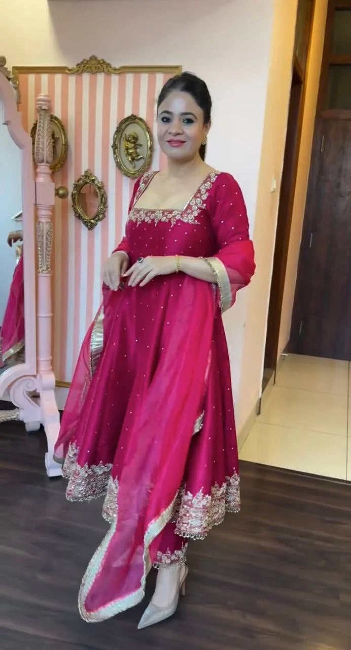 Woman in a red traditional outfit with white embroidery standing indoors.