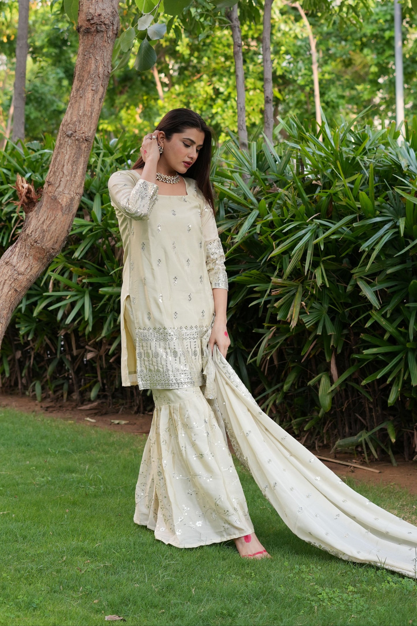 Woman in a traditional outfit standing outdoors with greenery in the background
