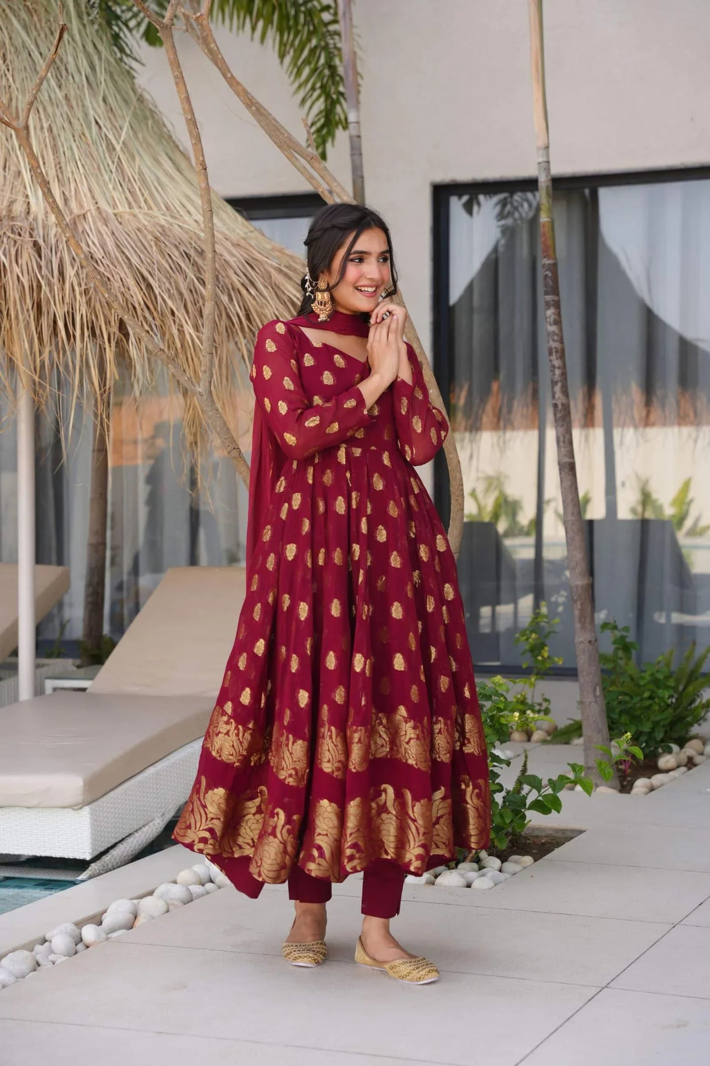 Woman in a red and gold dress standing outdoors near a poolside area.