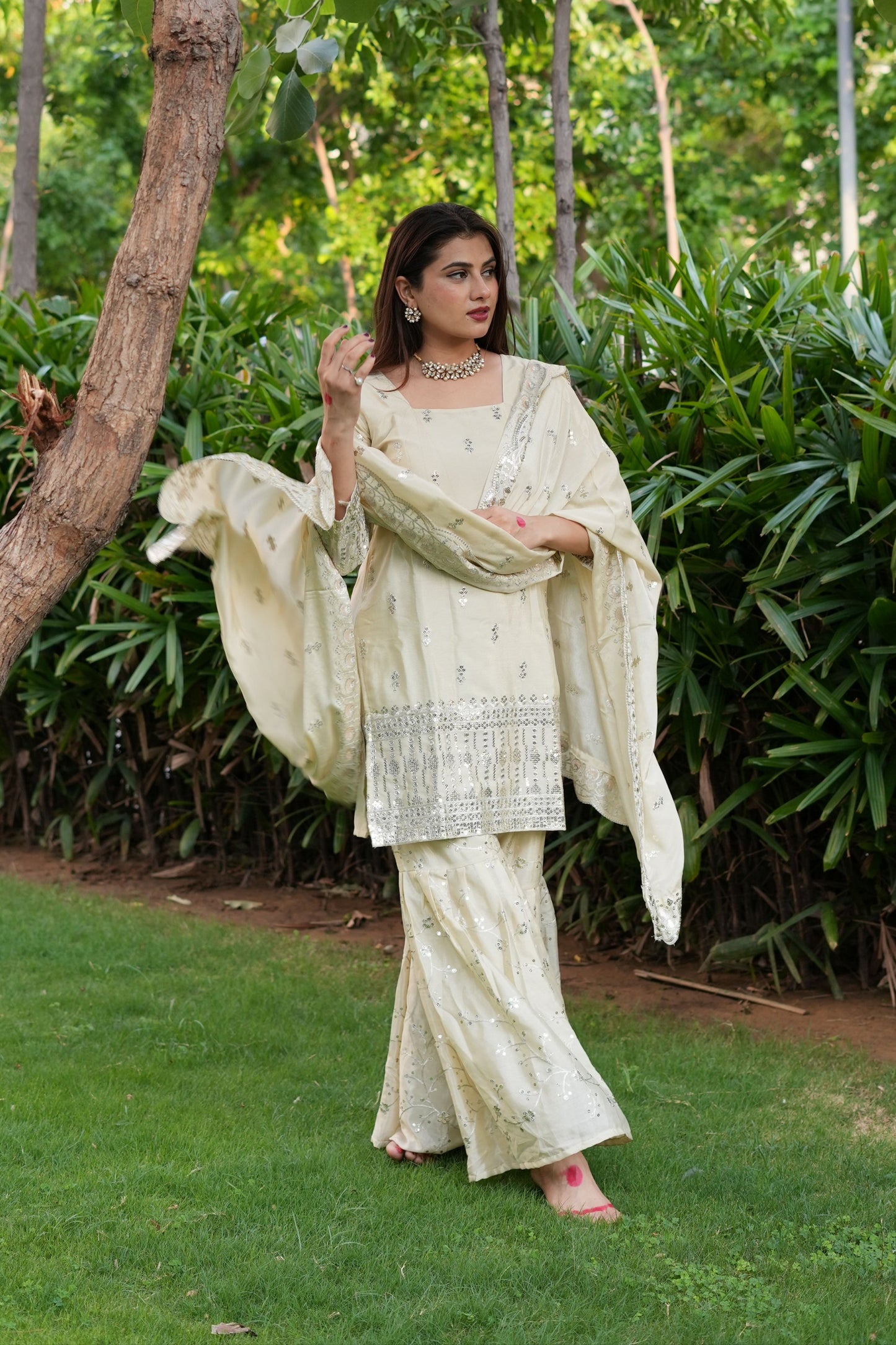 Woman in a traditional outfit standing outdoors with greenery in the background