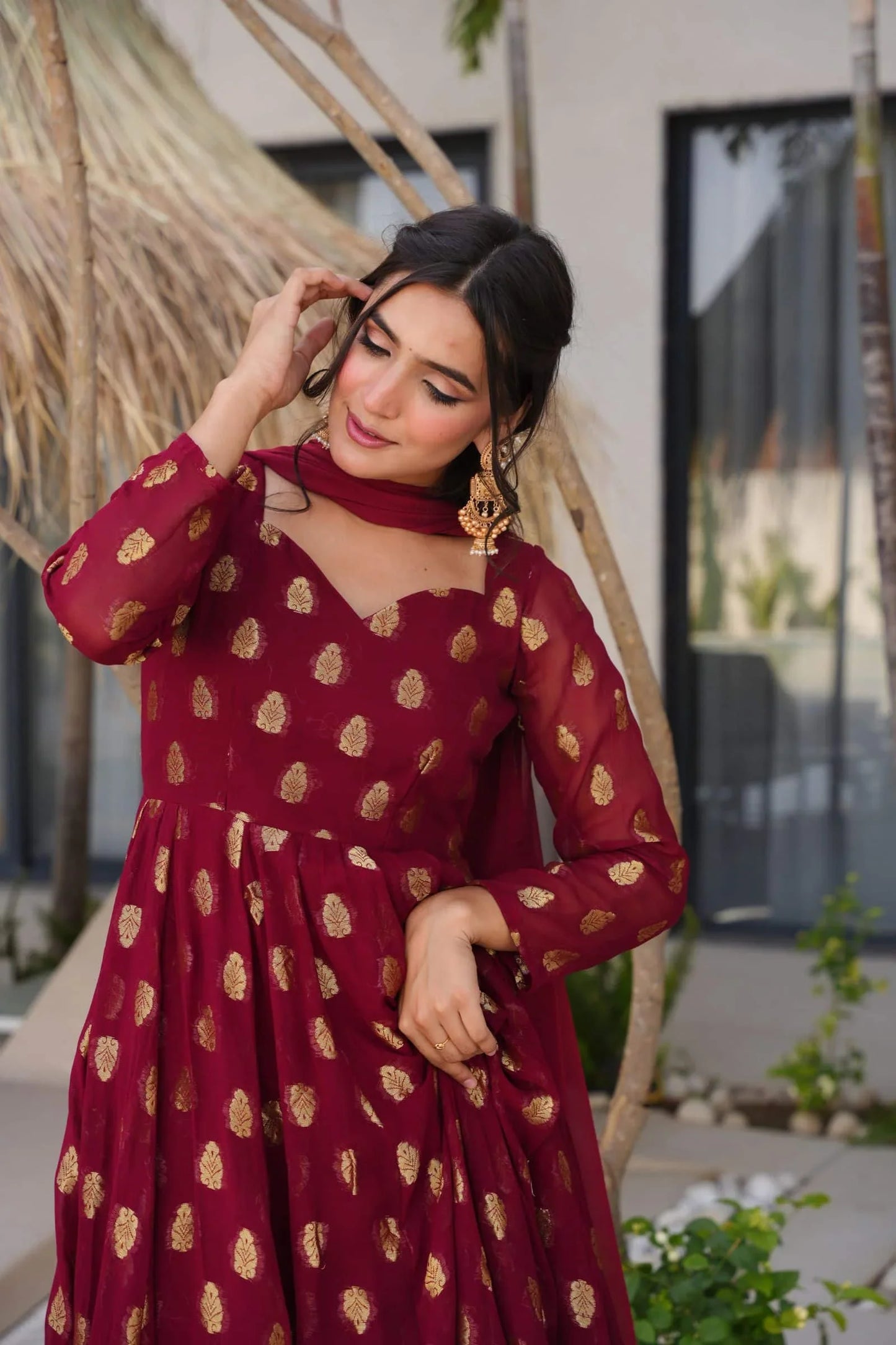 Woman wearing a maroon dress with gold patterns outdoors.