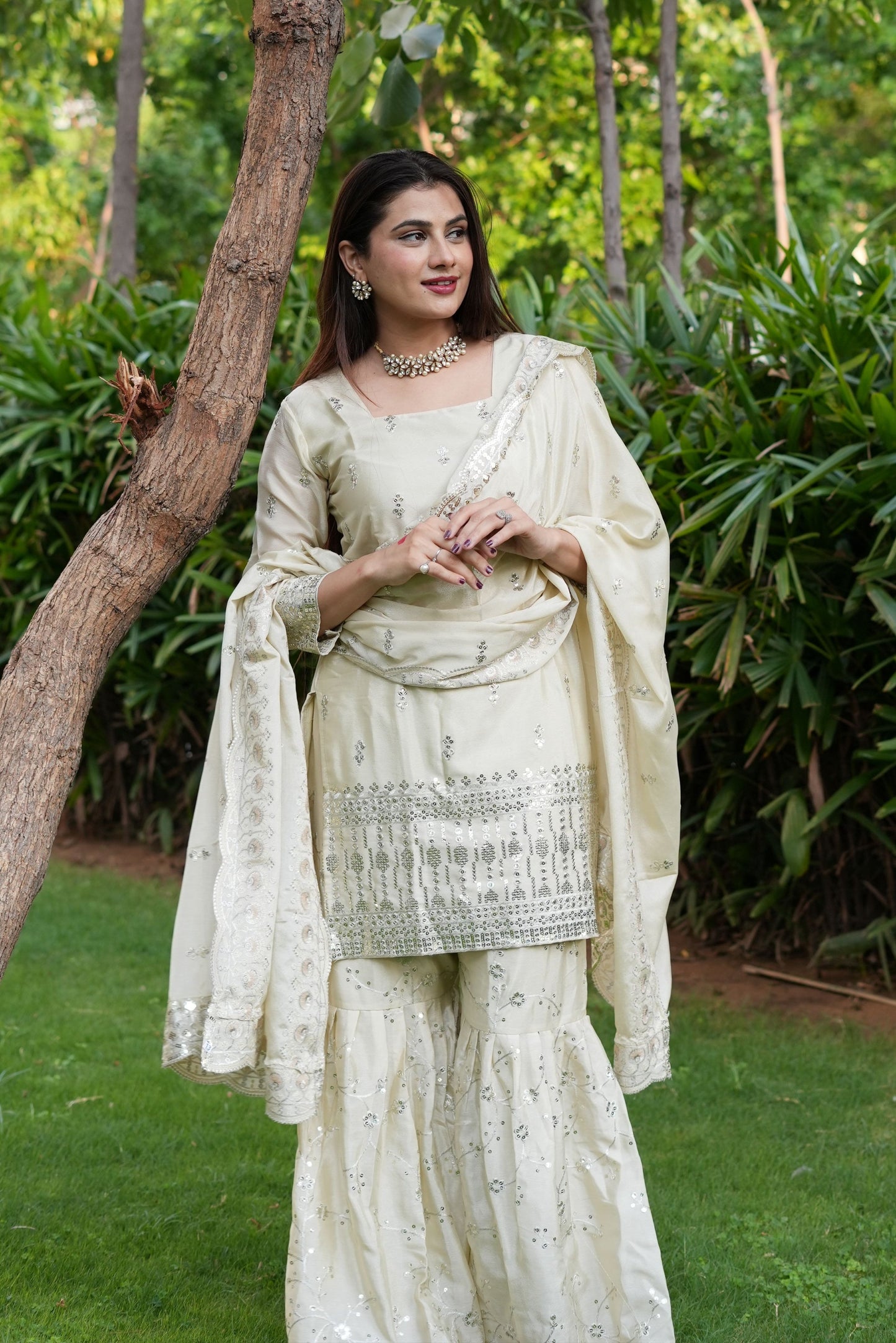 Woman in a traditional outfit standing outdoors with greenery in the background