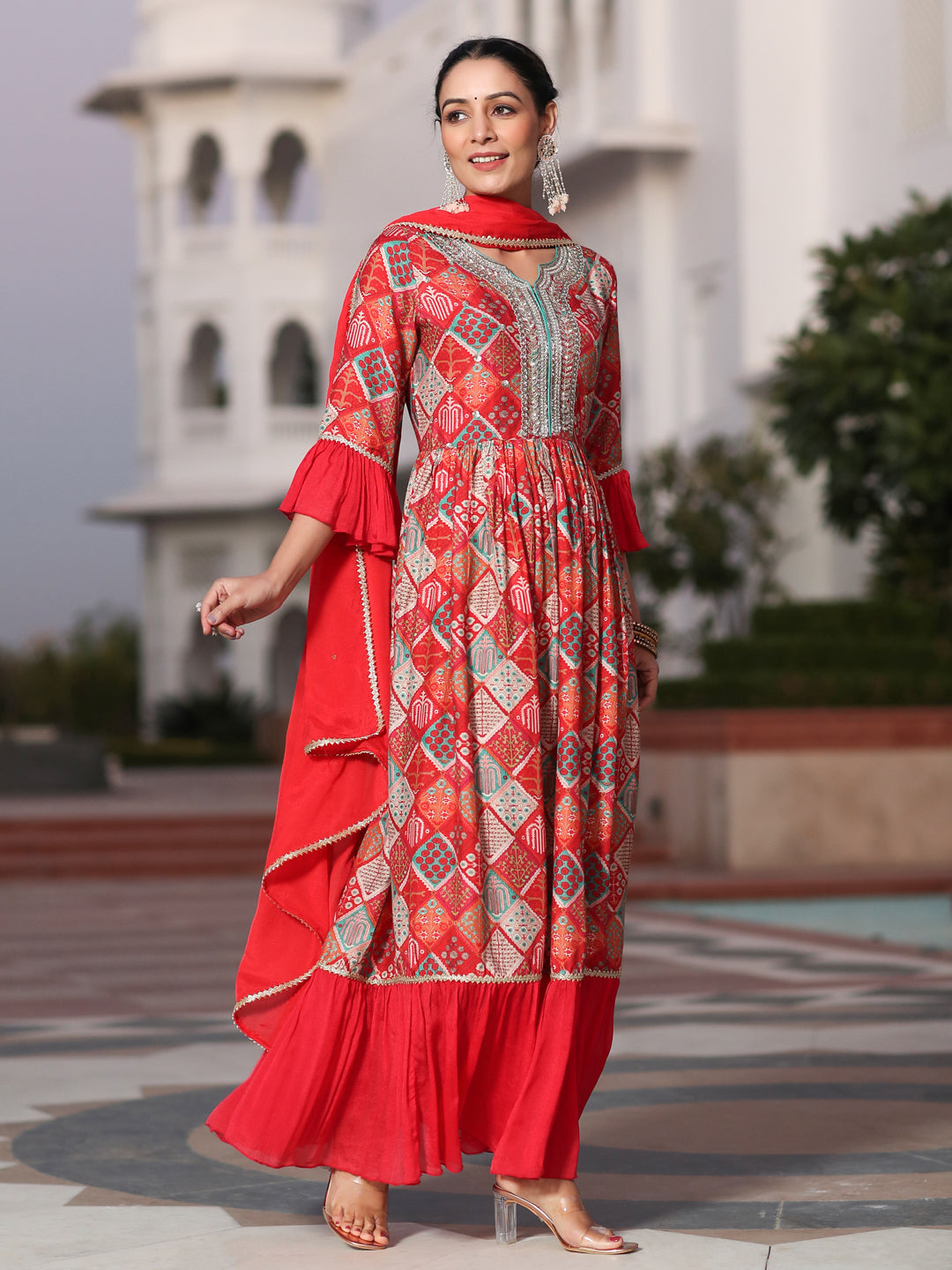 Woman in a red traditional outfit standing in front of a white architectural structure.