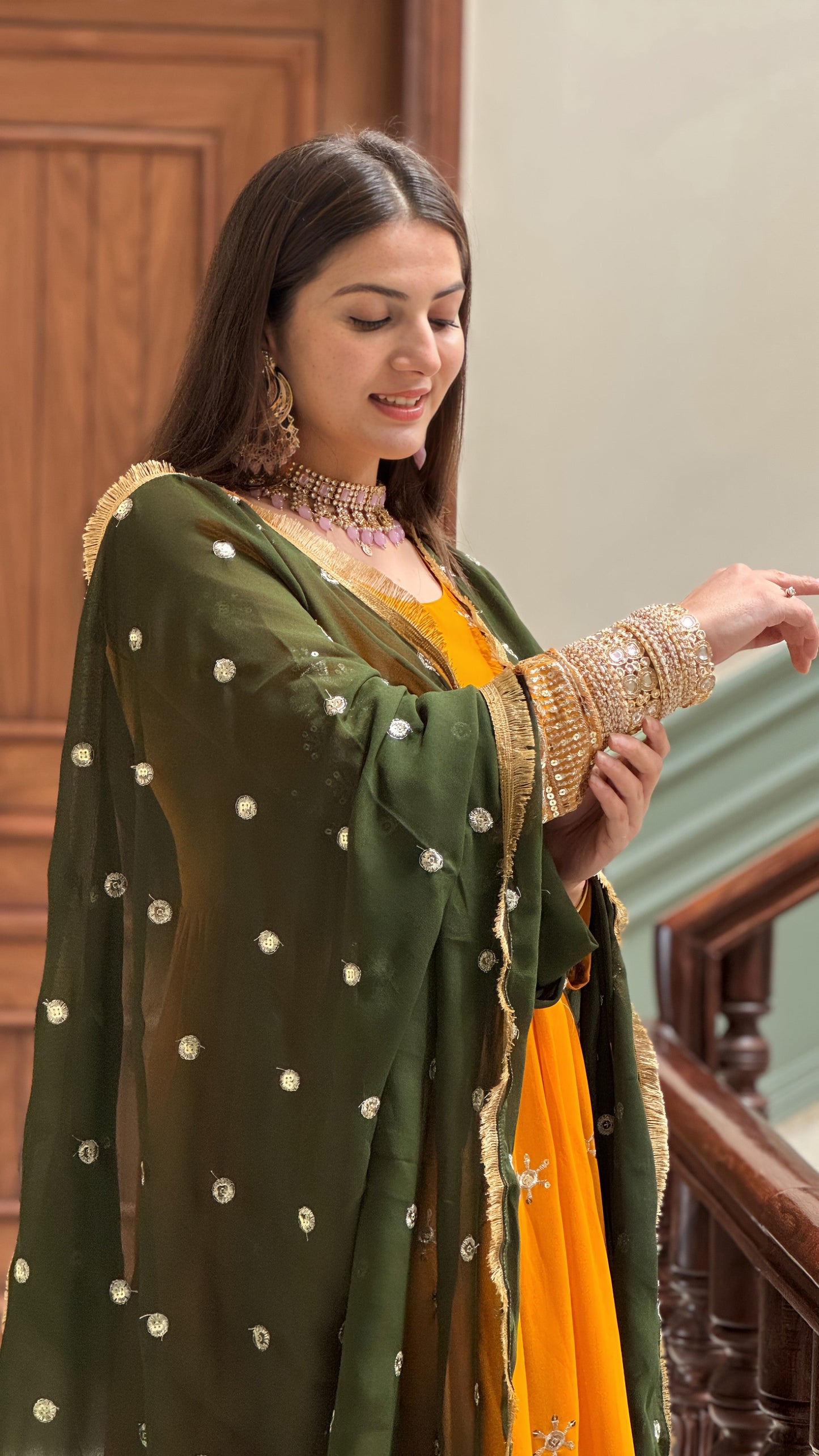 Woman in traditional green and yellow outfit with gold jewelry indoors.