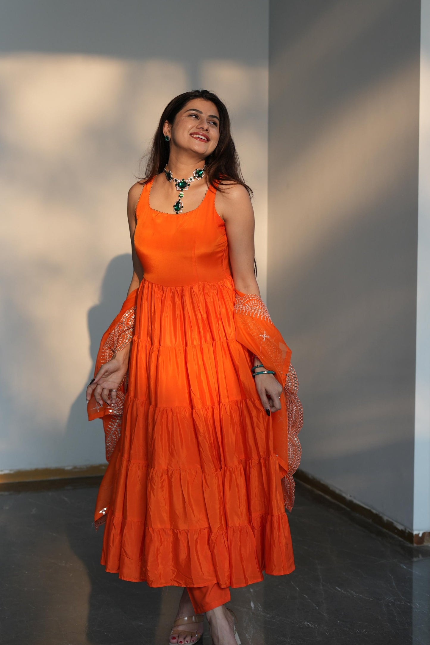 Woman wearing an orange dress standing against a plain wall.