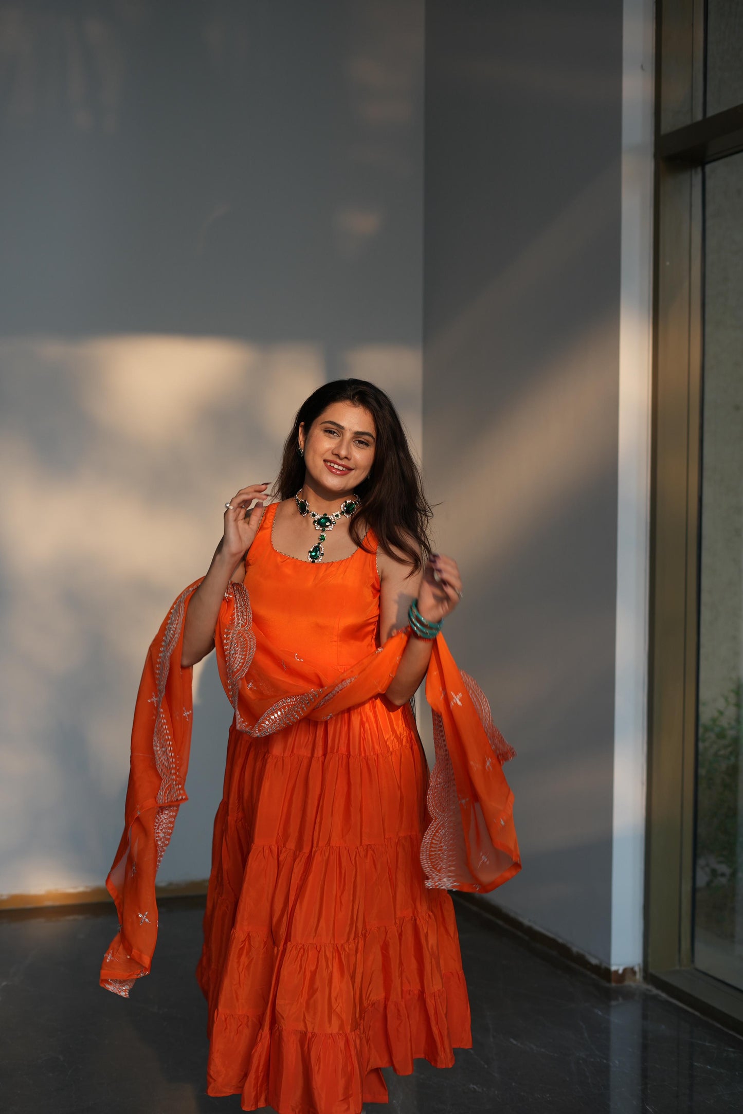 Woman in an orange dress standing against a light-colored wall.