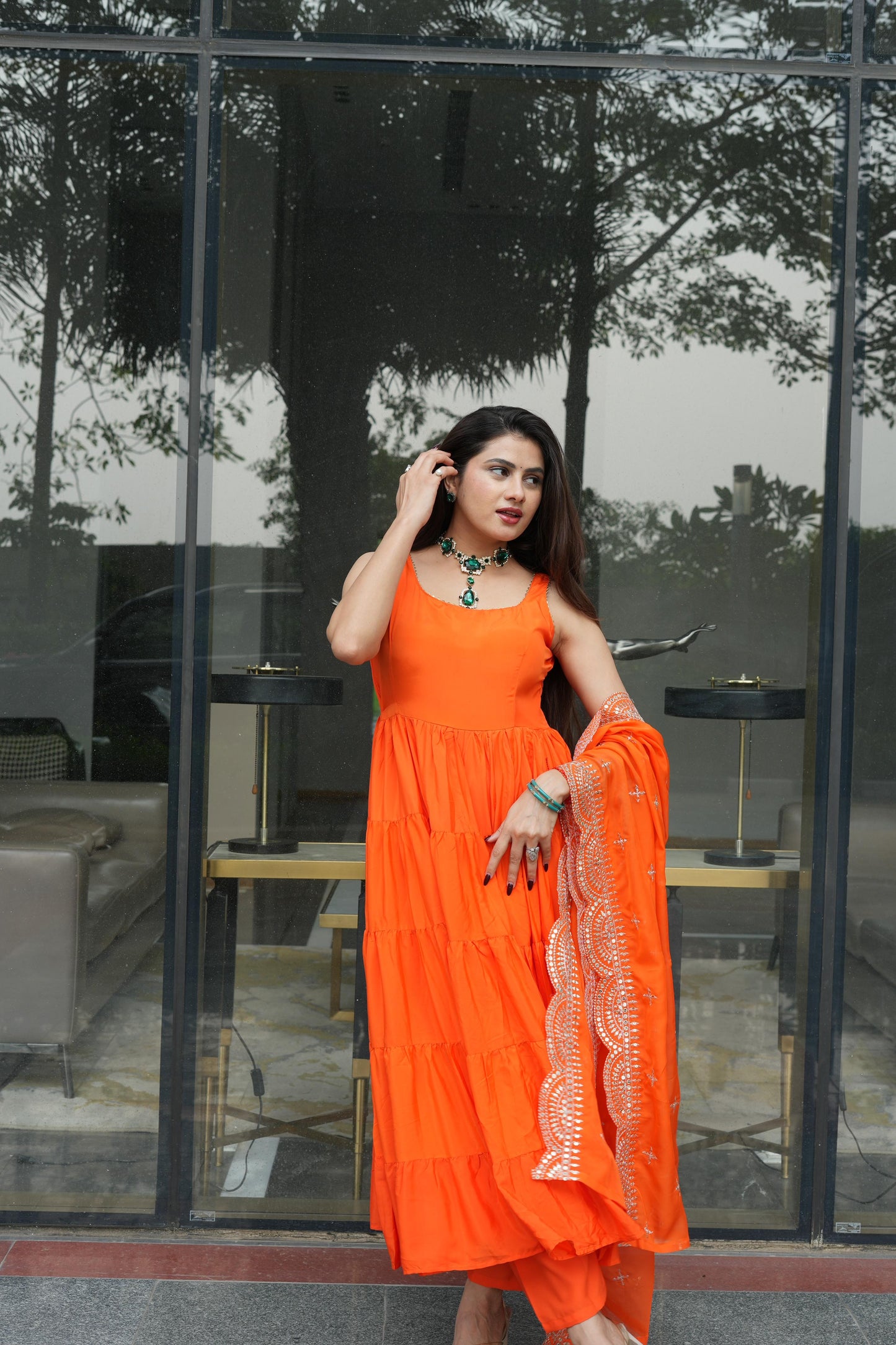 Woman in an orange dress standing in front of a glass wall with reflections.
