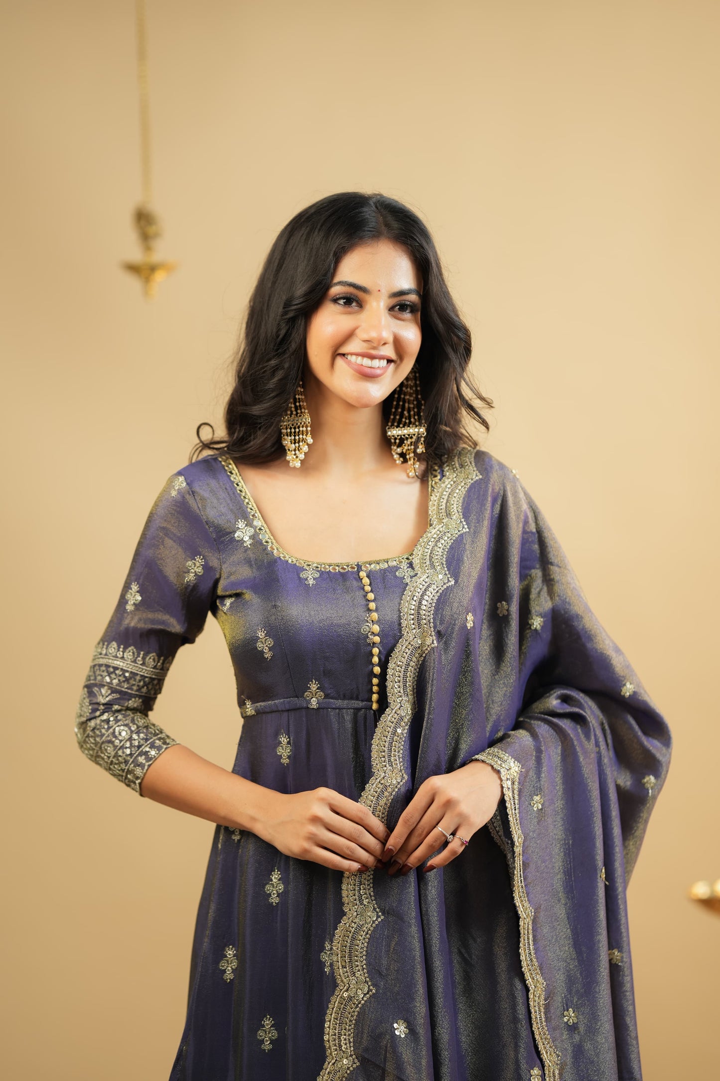 Woman wearing a purple dress with gold embroidery against a beige background
