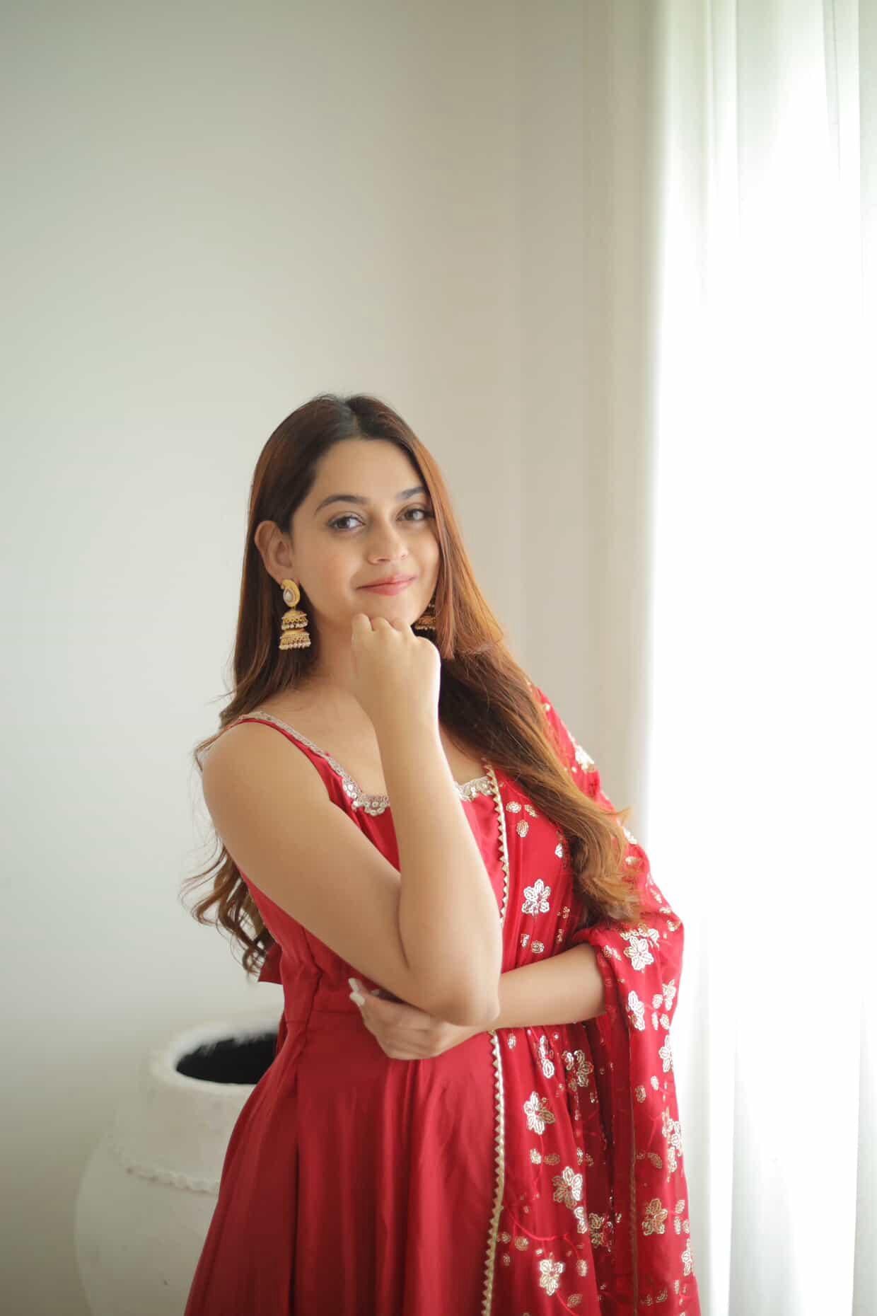 Woman in a red dress with floral patterns standing indoors.