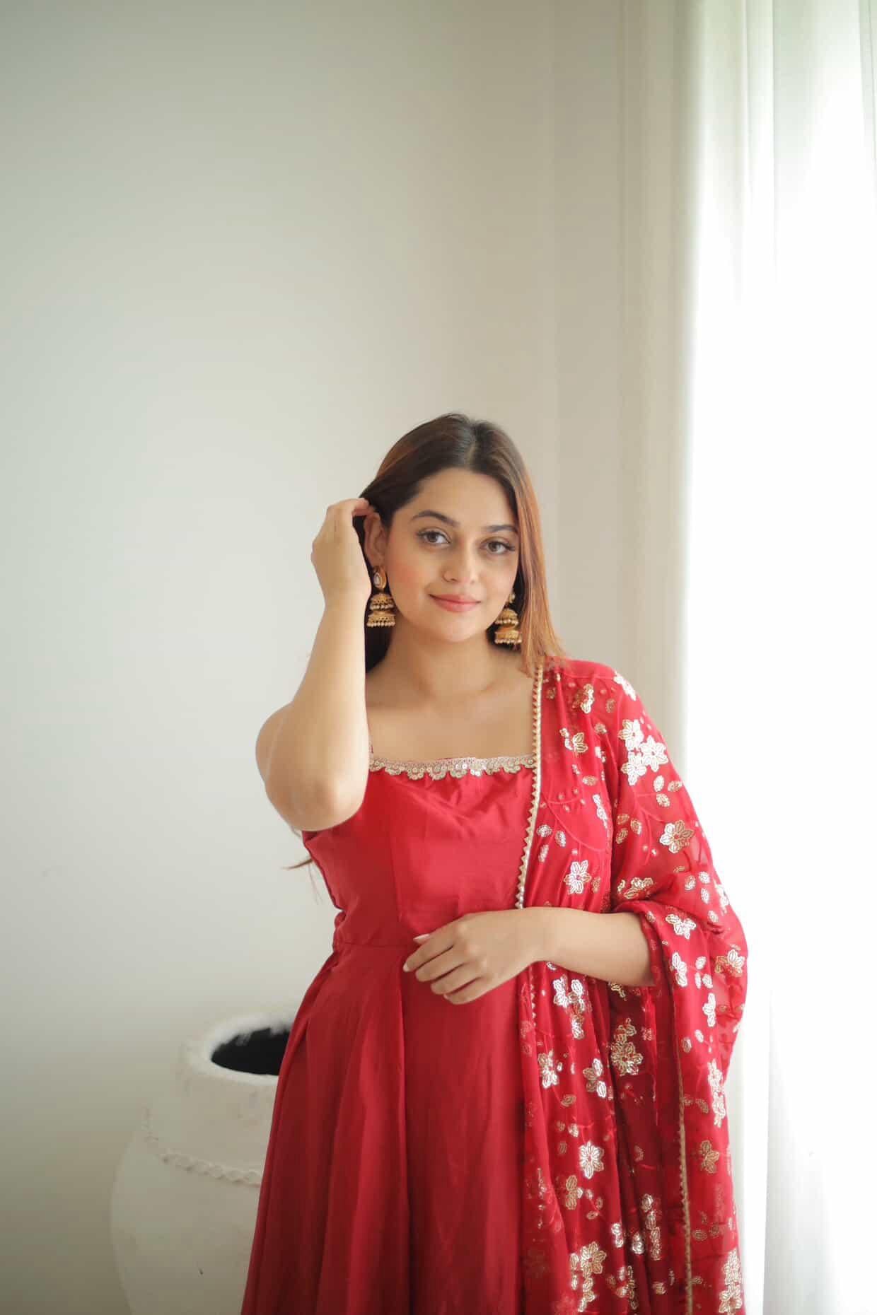Woman in a red dress with a floral dupatta against a white wall