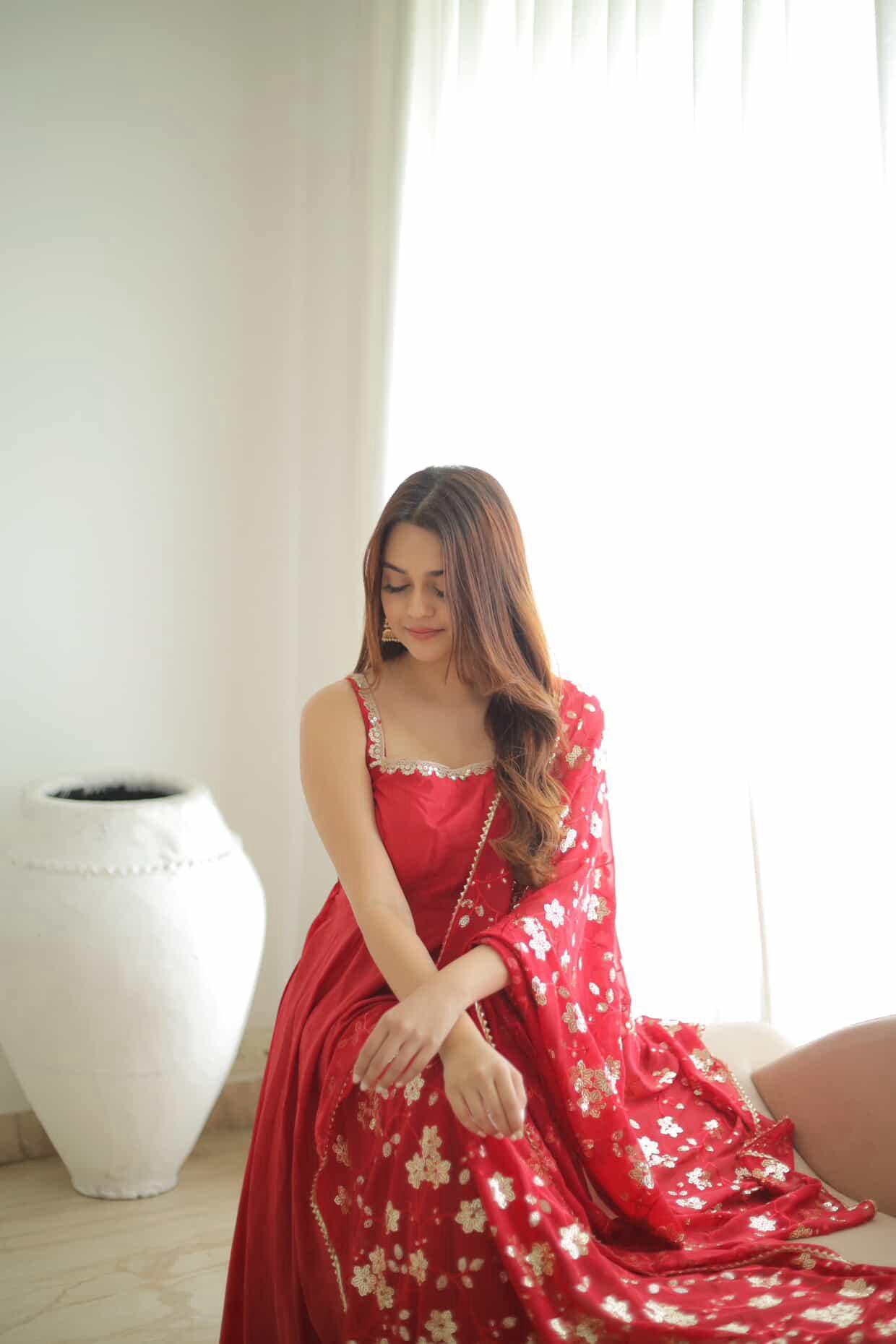 Woman in a red floral dress sitting indoors with a neutral background