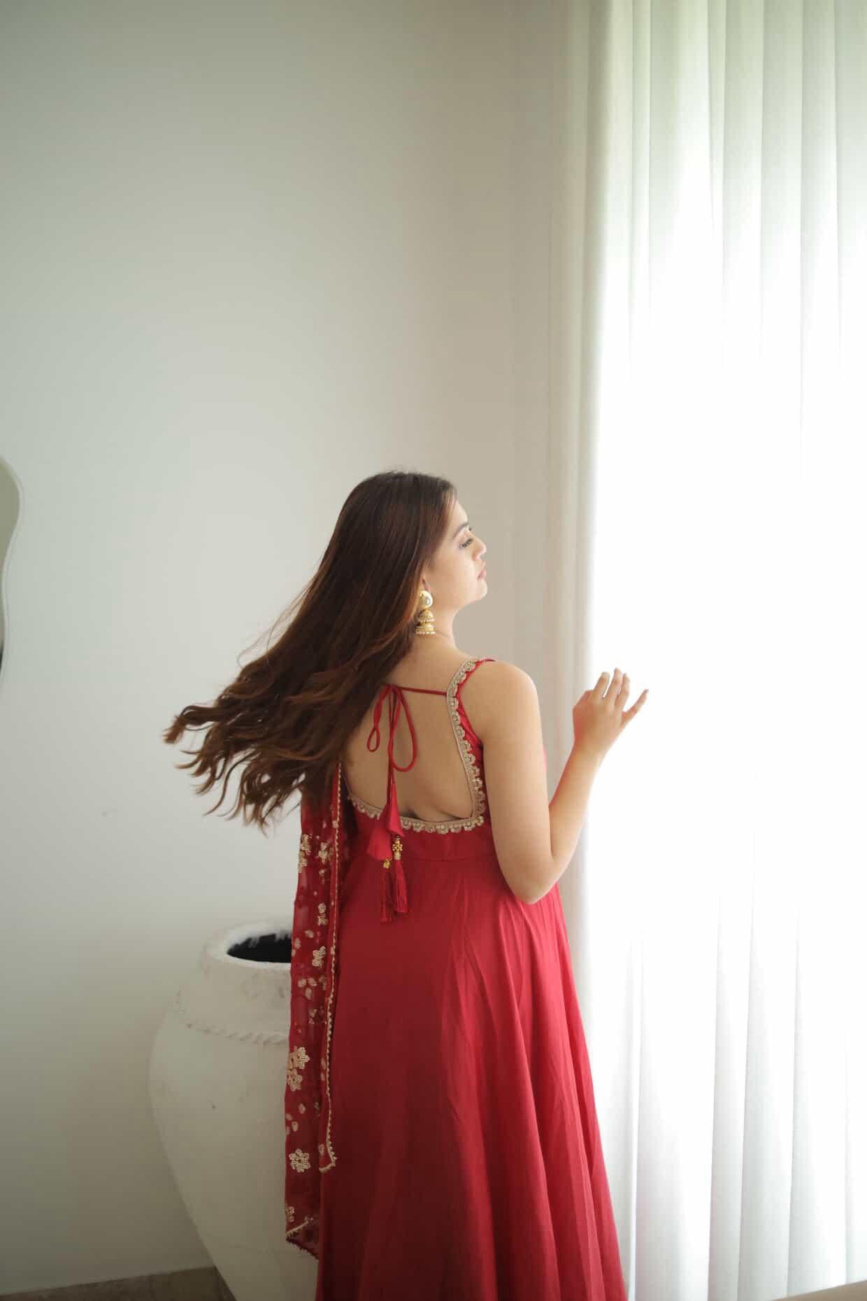 Woman in a red dress standing by a window with a white curtain