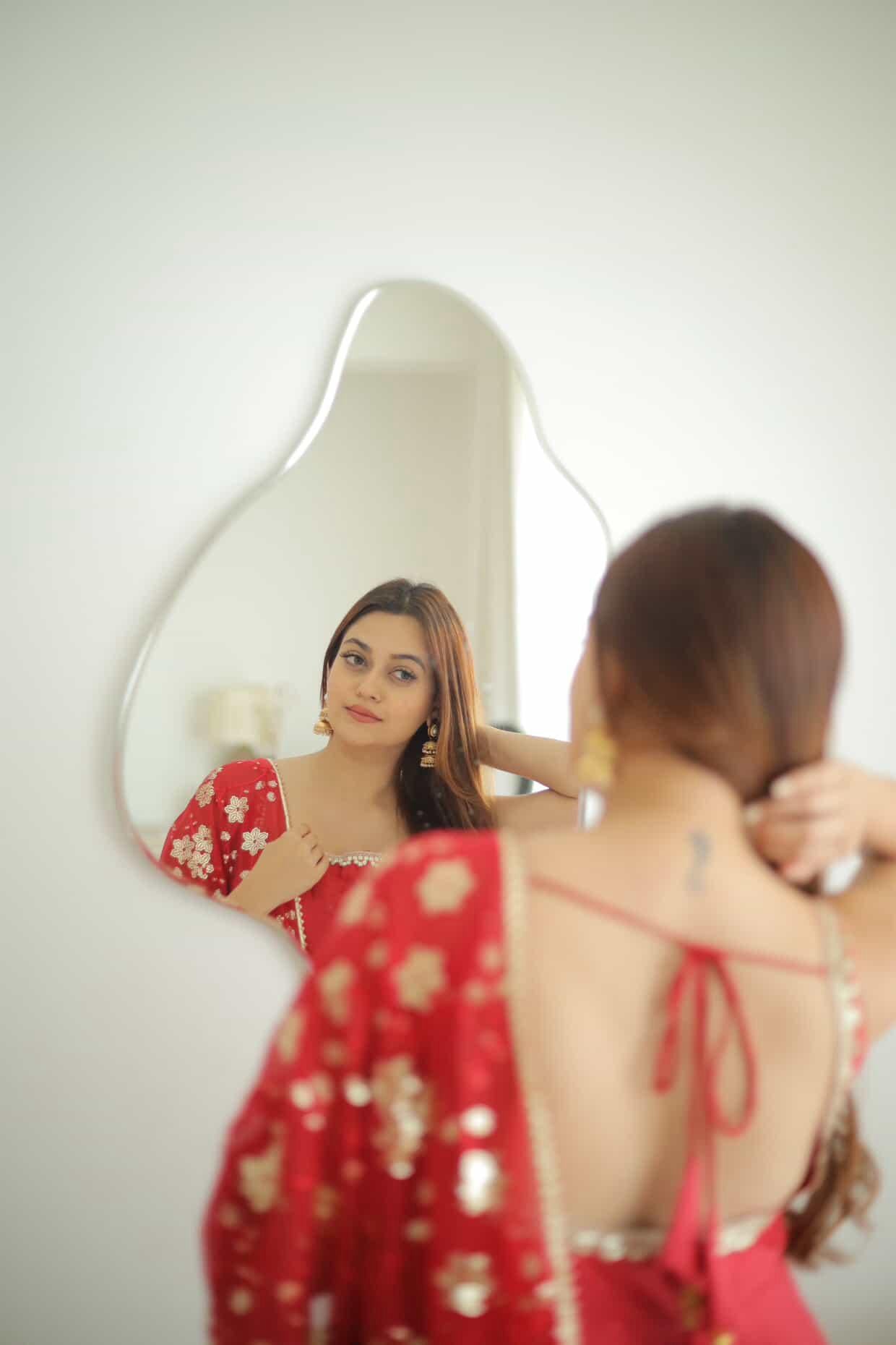 Woman in a red dress looking at herself in a mirror.