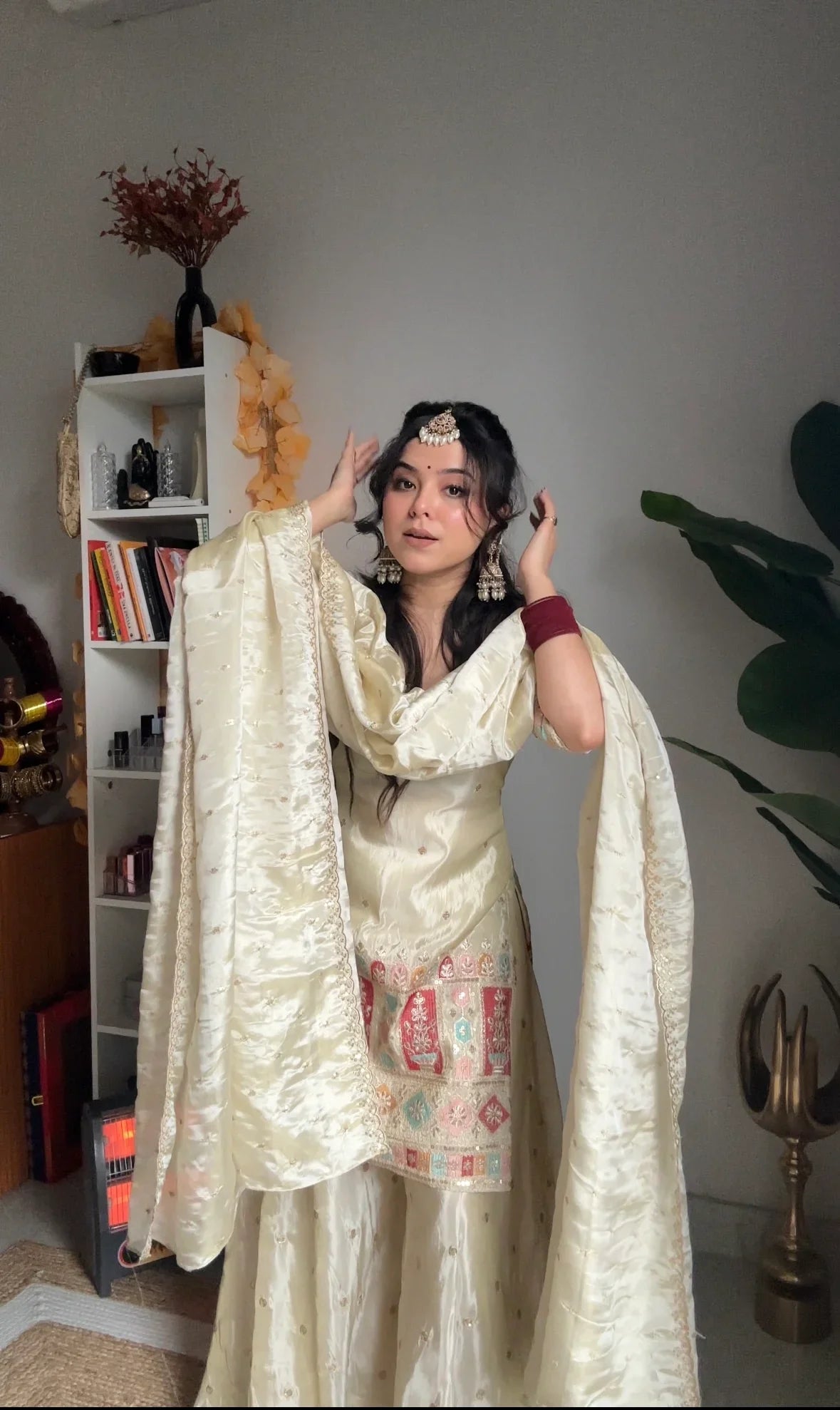 Woman in a traditional outfit standing in a room with decor elements.