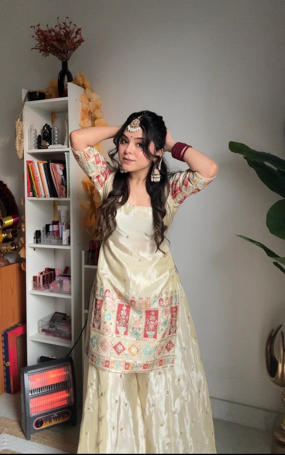Woman in traditional outfit posing in a room with a bookshelf and decorative items.