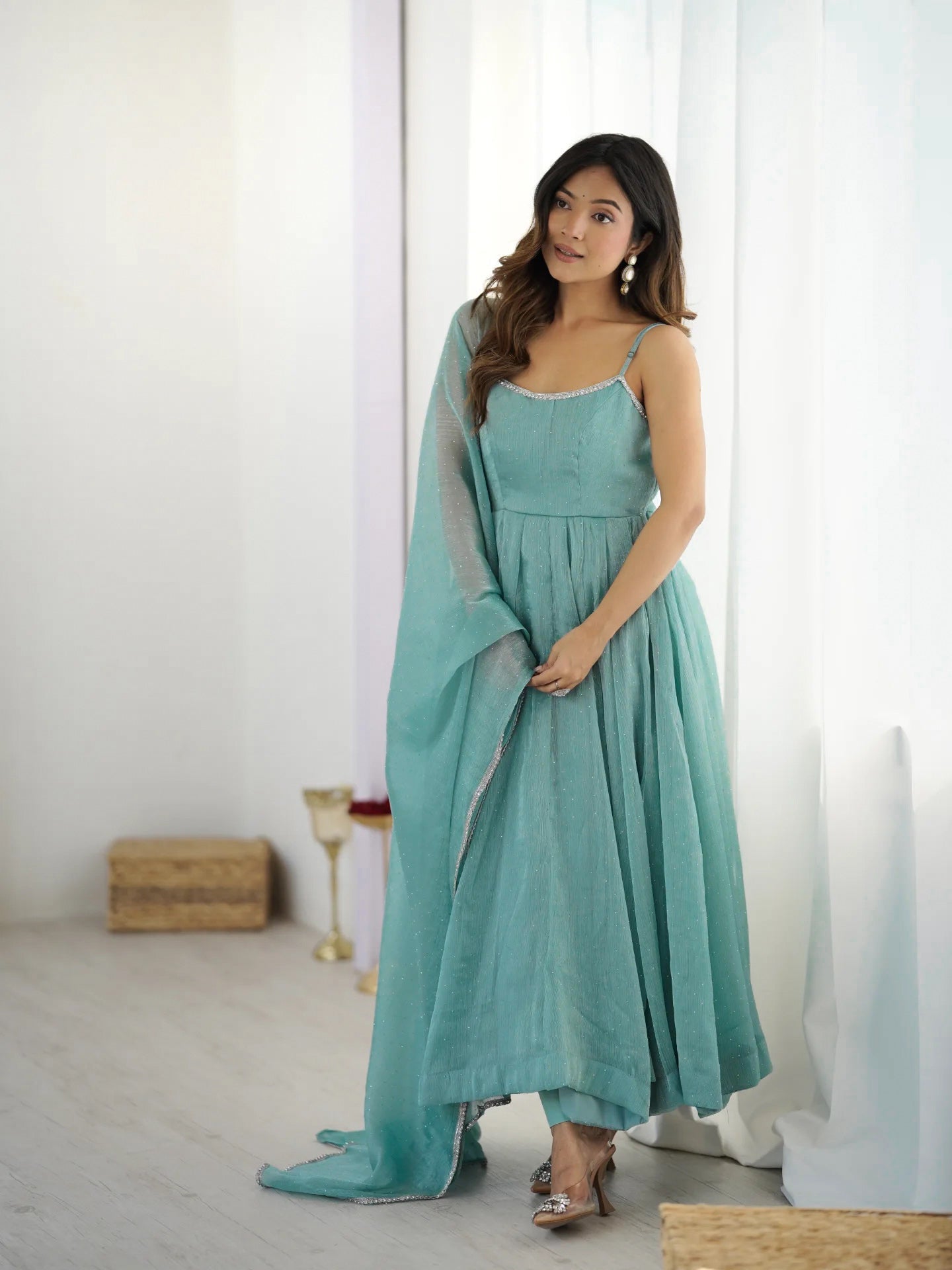 Woman wearing a teal dress with a matching shawl in a minimalistic room.