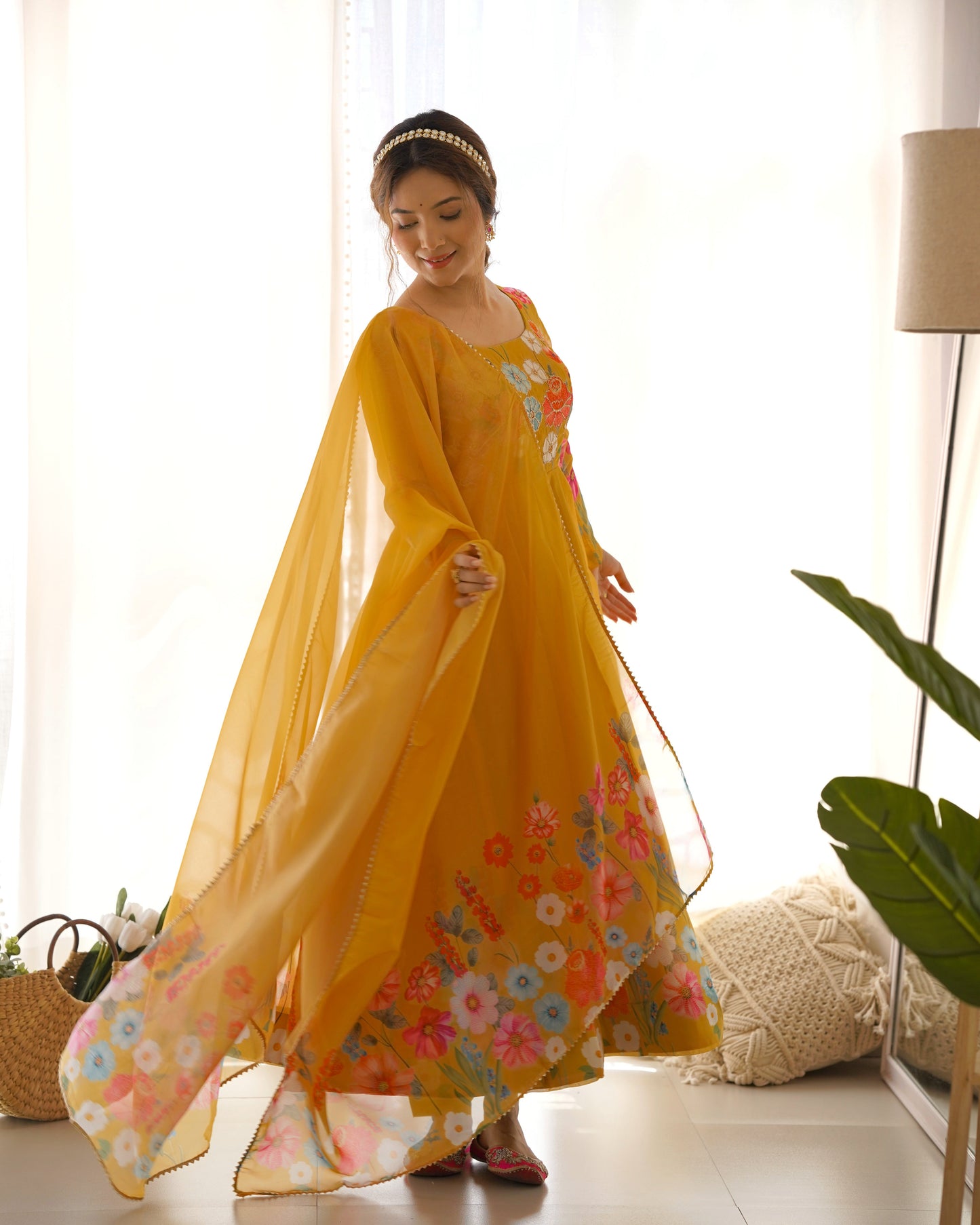 Woman wearing a yellow floral dress in a bright room with white curtains and a plant.