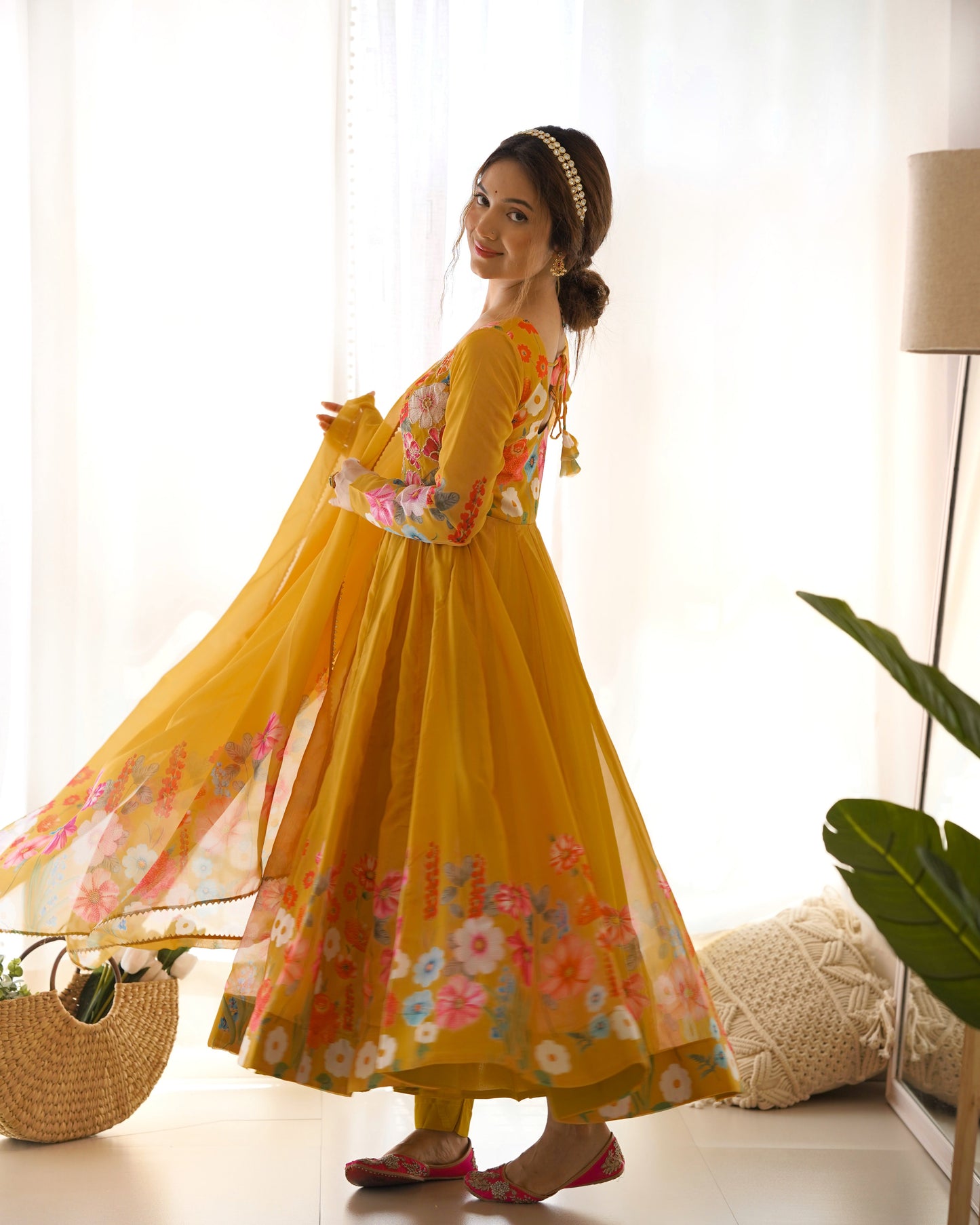 Woman wearing a yellow floral dress in a bright room with white curtains and a plant.