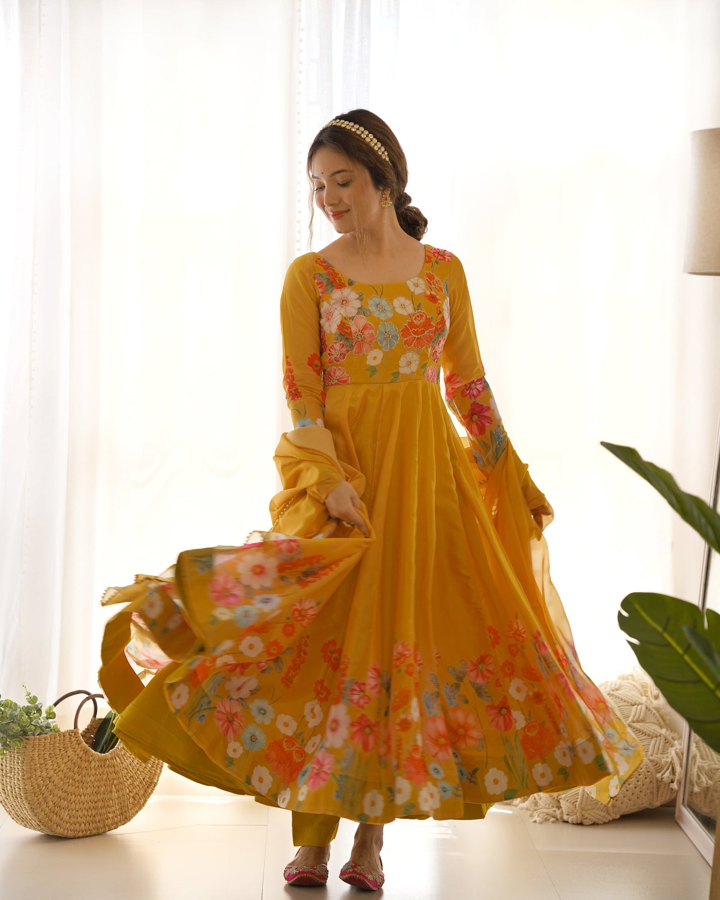 Woman wearing a yellow floral dress in a bright room with white curtains and a plant.