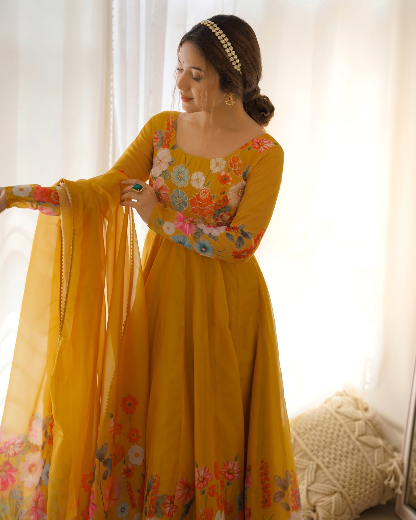 Woman wearing a yellow floral dress holding a dupatta against a white curtain background