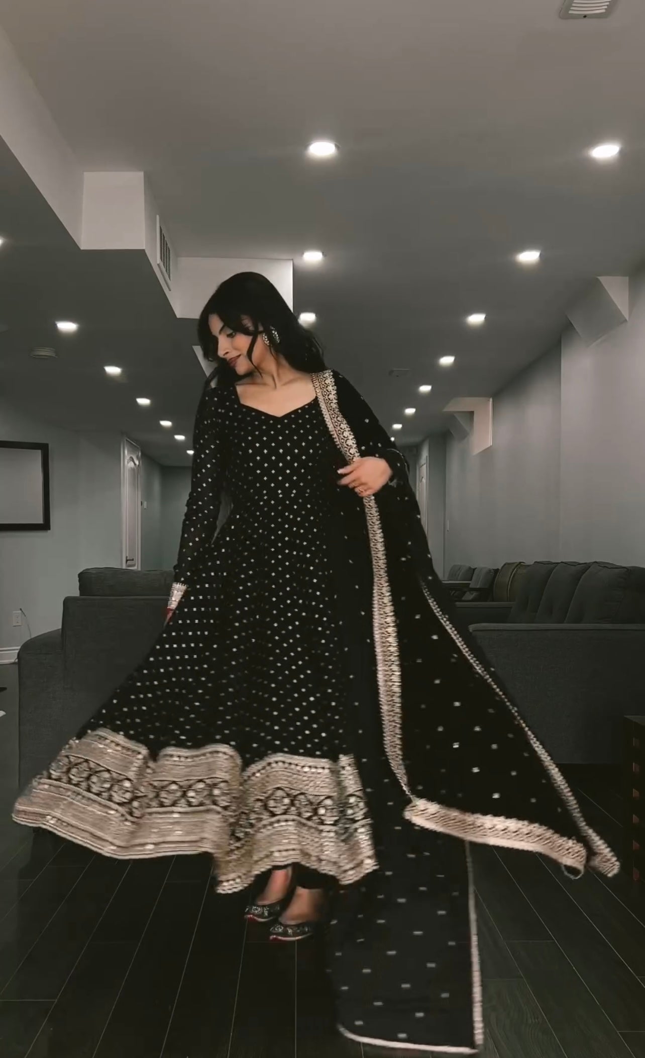 Woman wearing a black traditional outfit with white patterns in an indoor setting.