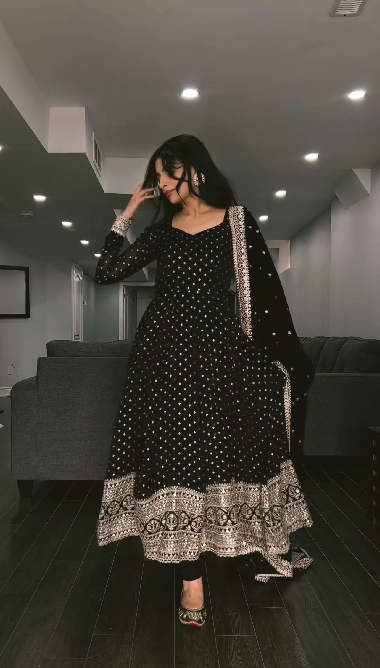 Woman wearing a black and white patterned outfit in a modern living room.