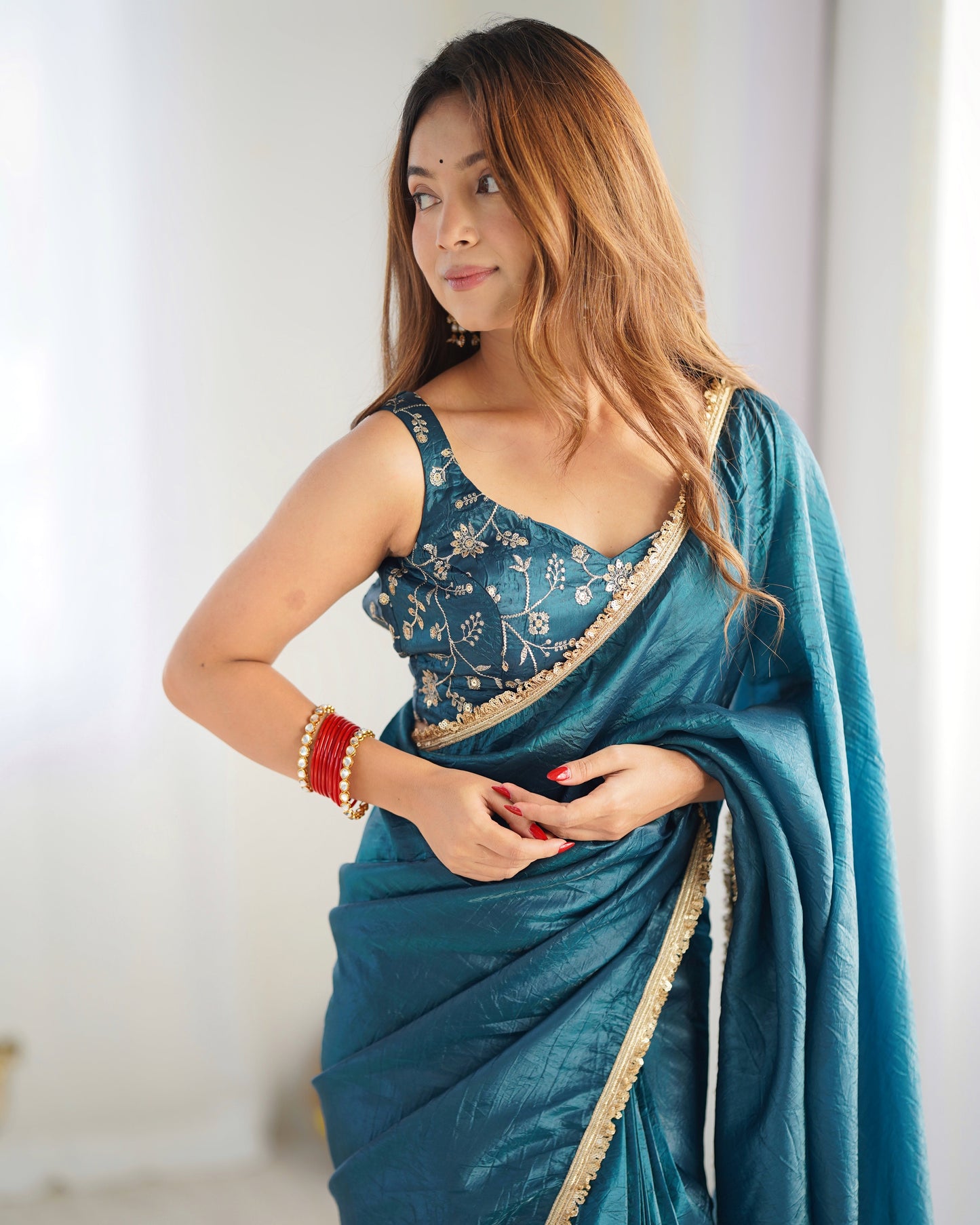Woman wearing a blue saree with a white blouse against a plain background