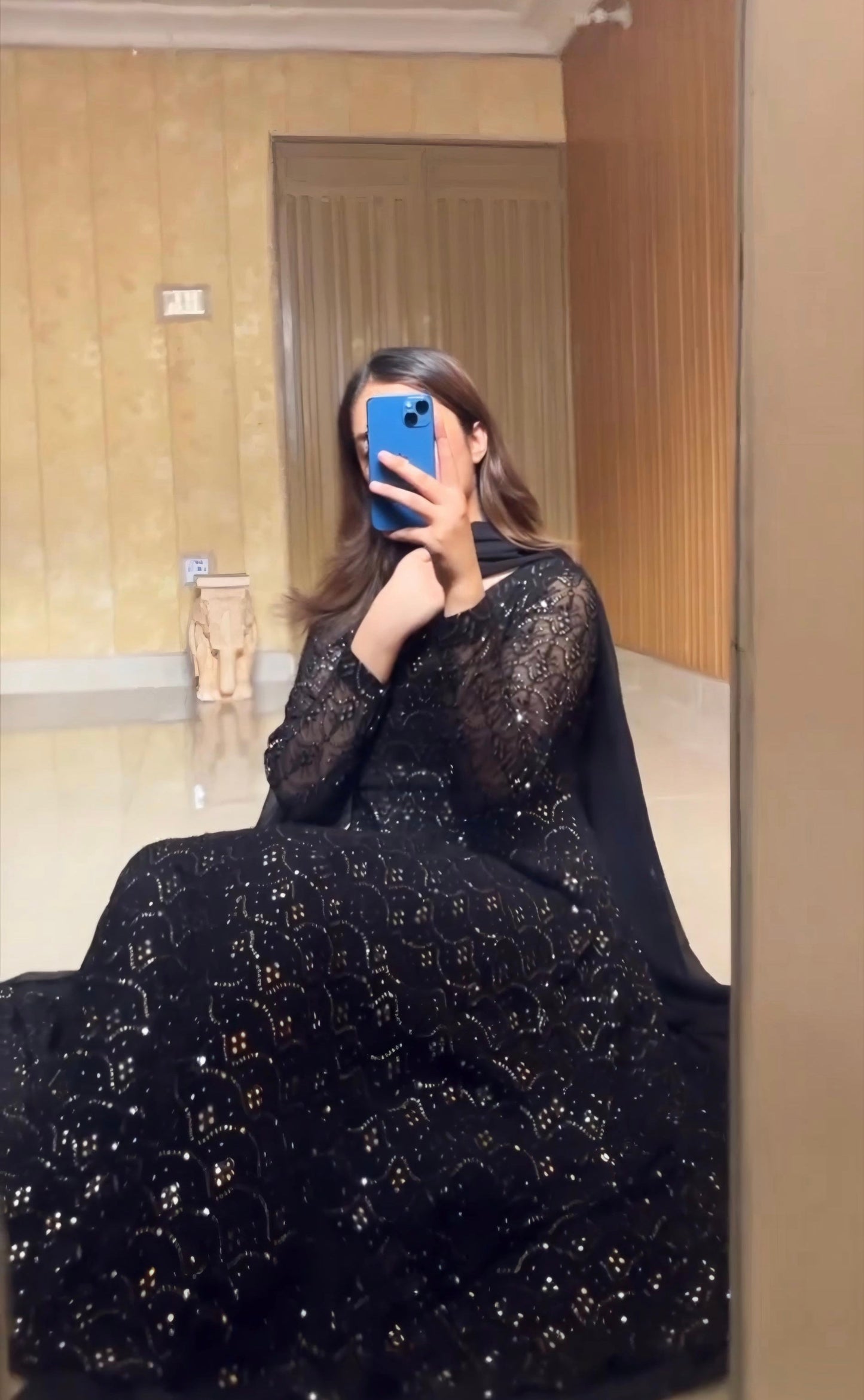 Person wearing a black dress with gold embroidery taking a mirror selfie.