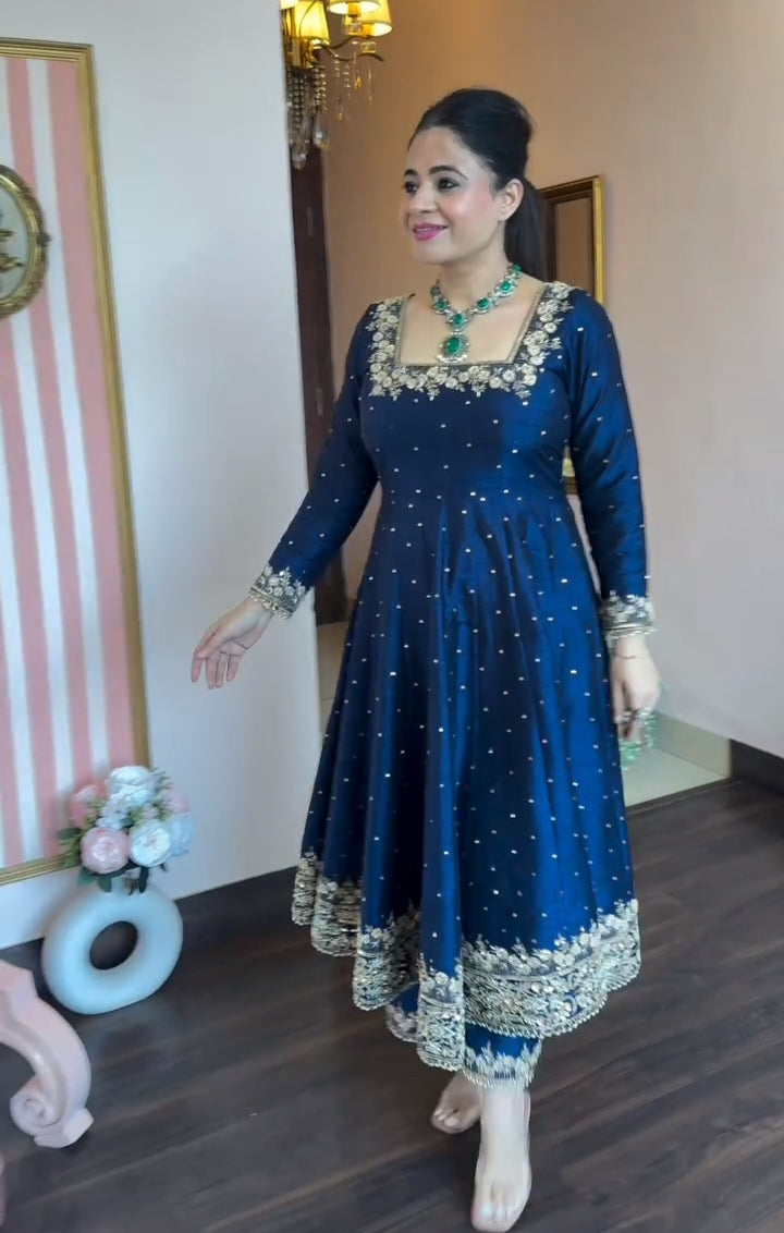 Woman in a blue traditional outfit with white patterns standing indoors.