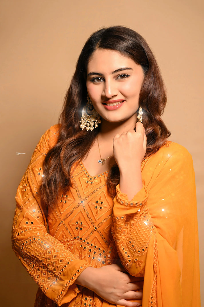 Woman wearing an orange traditional outfit with intricate designs on a beige background