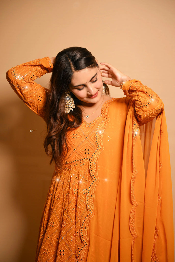 Woman wearing an orange embroidered outfit against a beige background