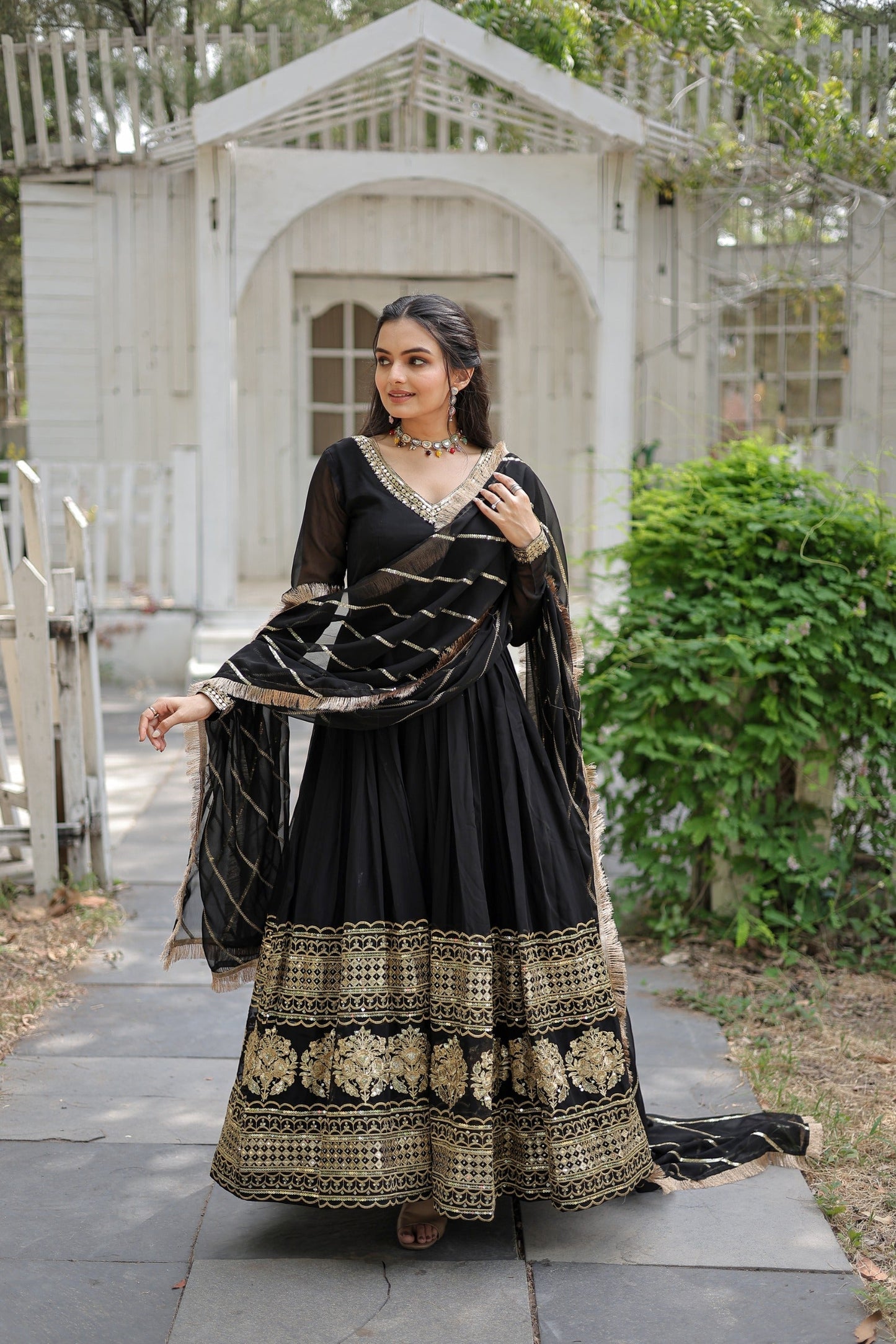Woman in a black and gold traditional outfit standing outdoors.