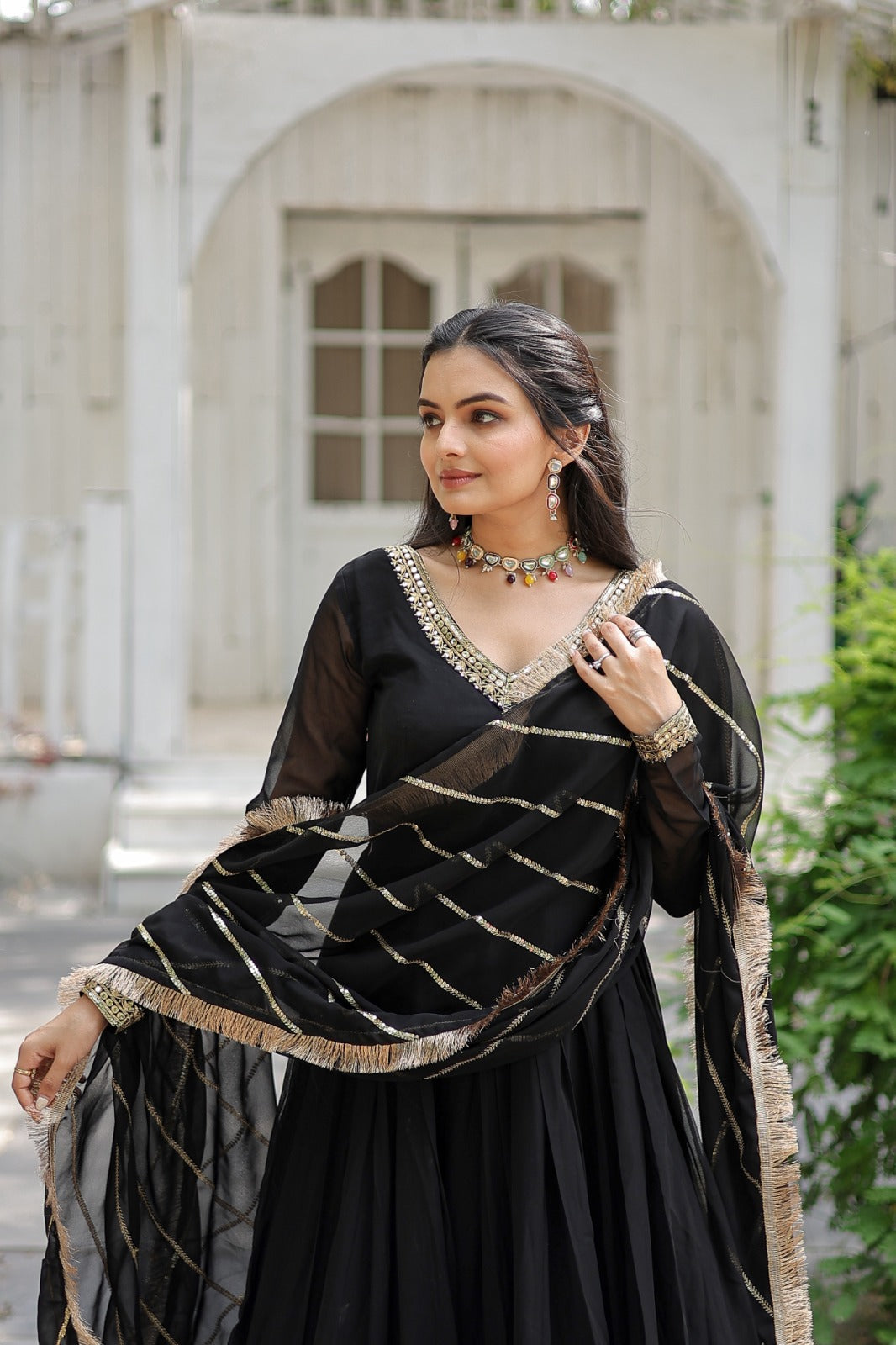 Woman in a black traditional outfit with gold details standing outdoors.