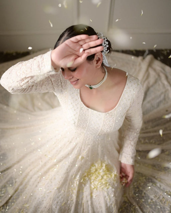 Woman in a white dress with long sleeves and a pearl necklace, surrounded by decorative elements.